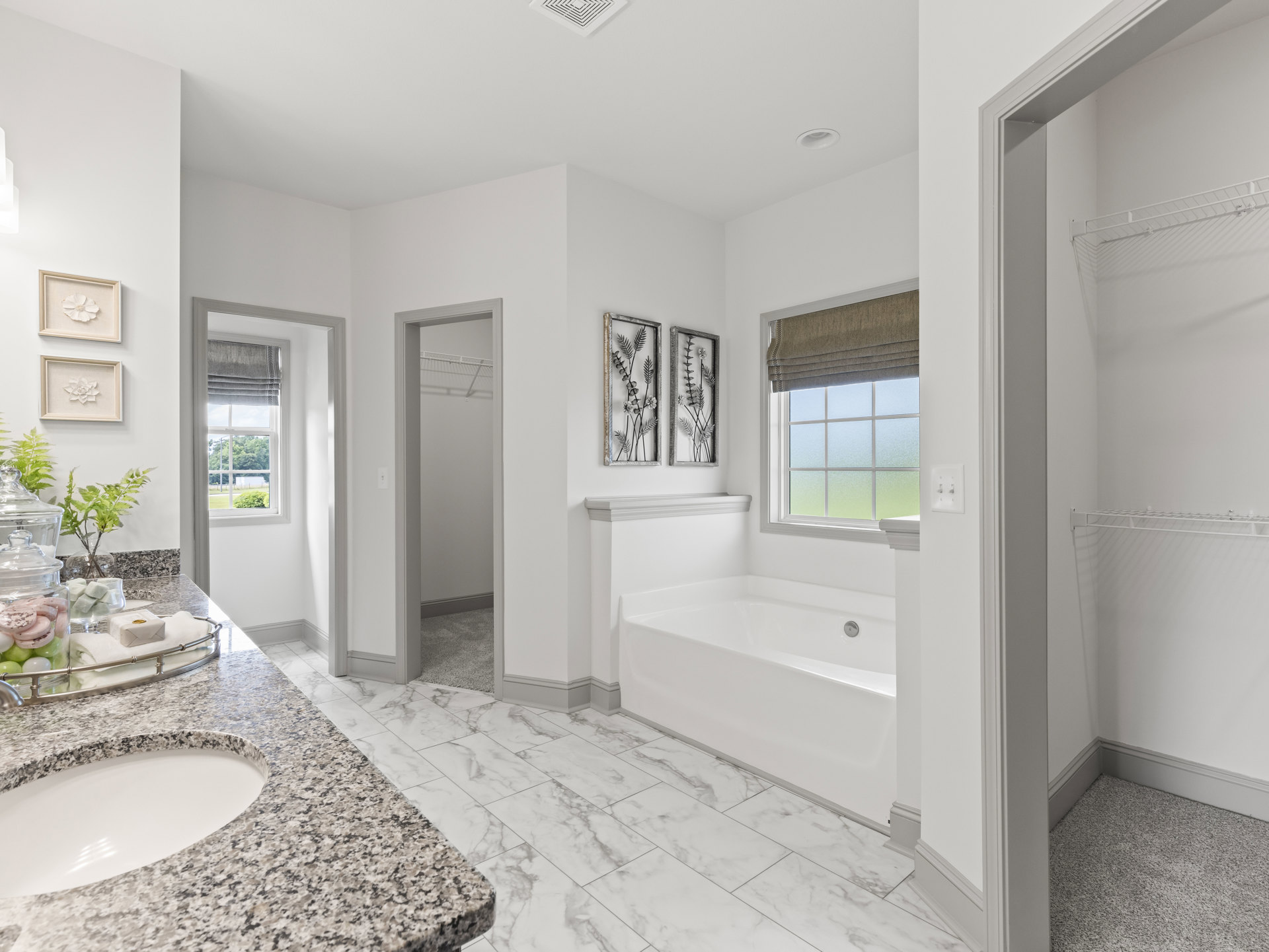 Bathroom with polished marble floor and marble countertop, white sink with black and white speckled surface, metal wall art, framed white flower, freestanding white bathtub, jar of