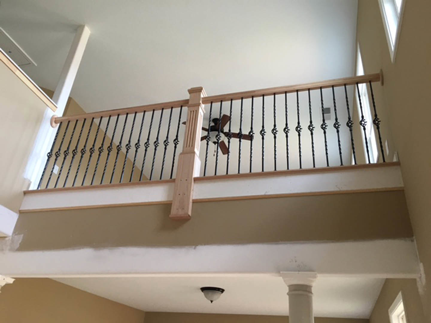Wooden staircase with metal railing, white pillar, ceiling fan with light fixture, and large window in a bright interior space