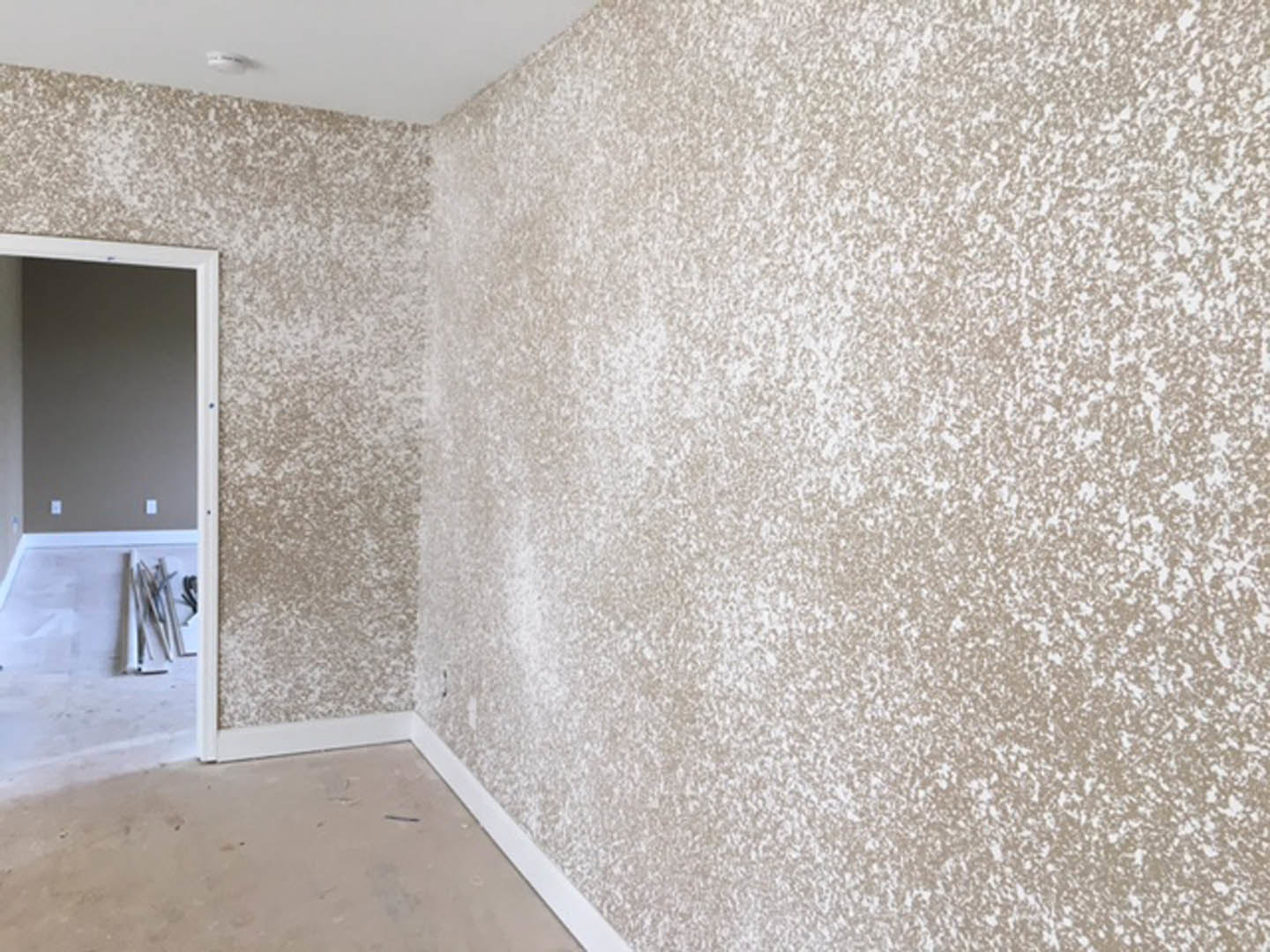 Bathroom with marble tile flooring, plaster walls with visible wiring and white specks, open door, person standing near wall, and blurred clock in background