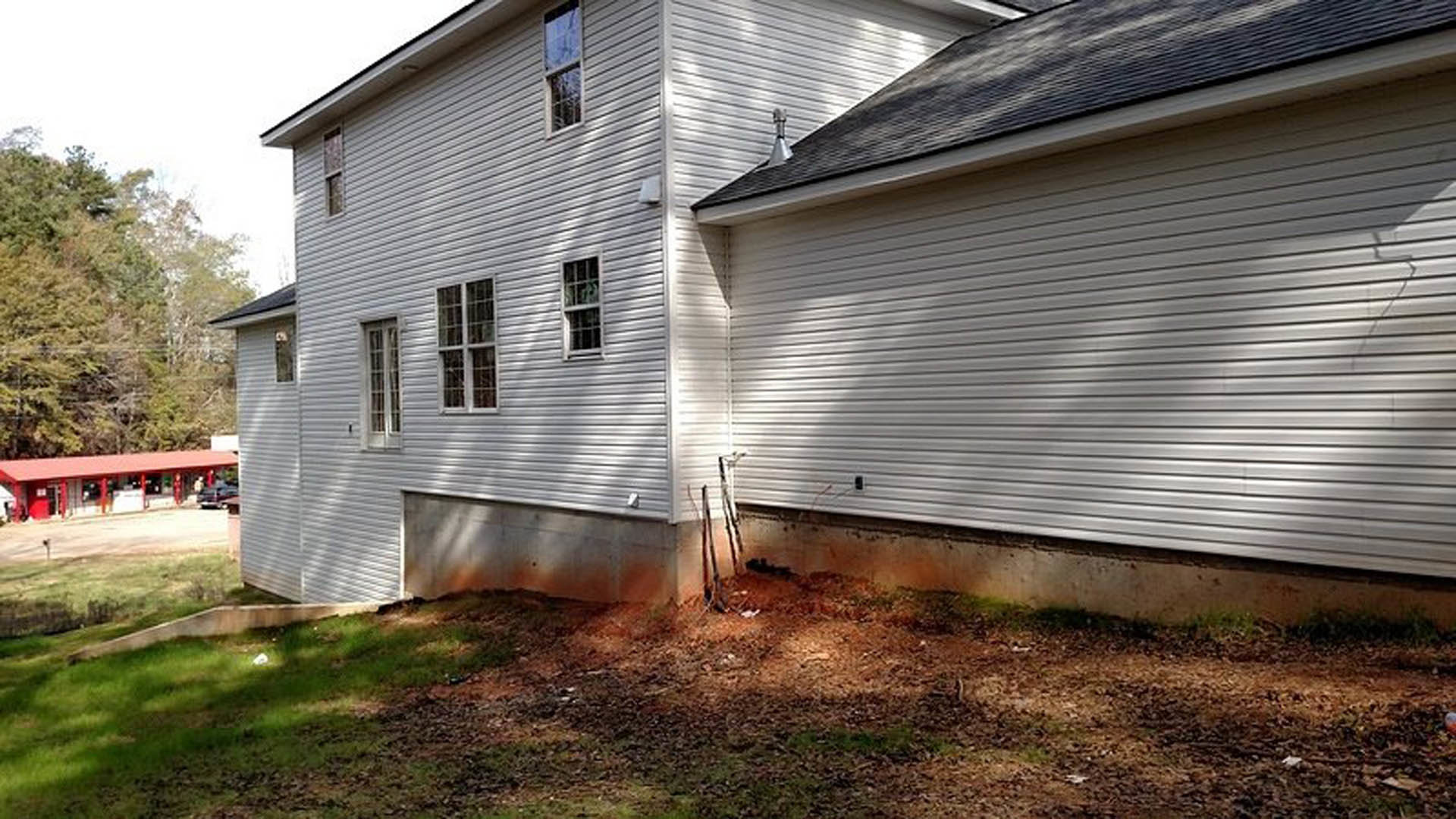 White two-story home with black roof, red pillars framing the entry, multi-pane windows, manicured green lawn, and mature trees in the yard