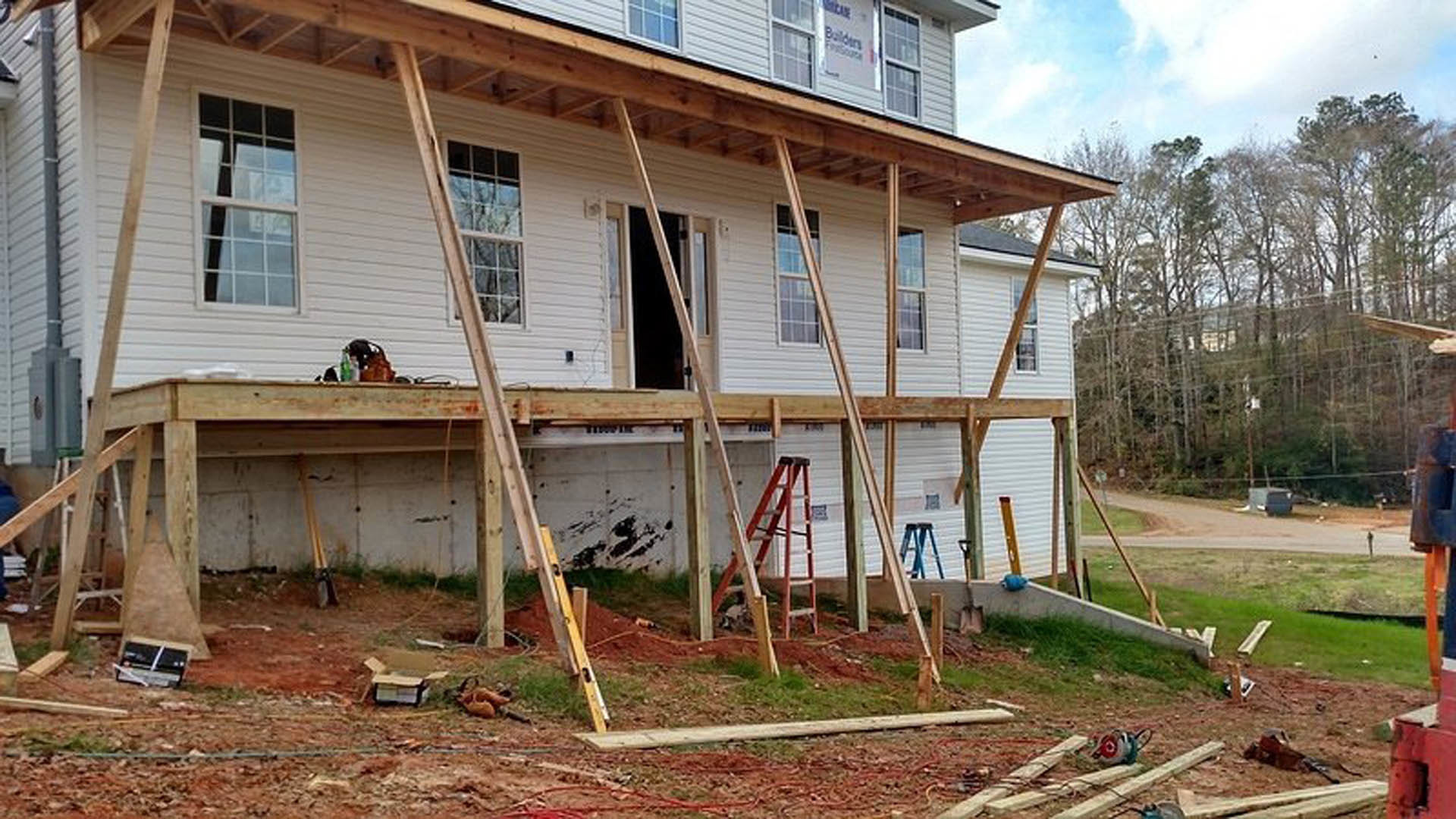 Framed house under construction with exposed lumber, square window, and wooden ladder leaning against exterior wall