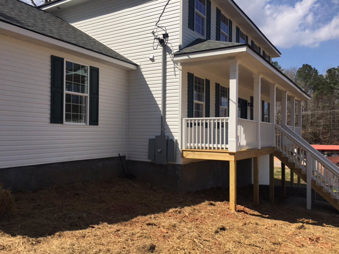 Two-story house with white siding, black shuttered windows, wooden porch featuring white railings, front steps, and manicured lawn.
