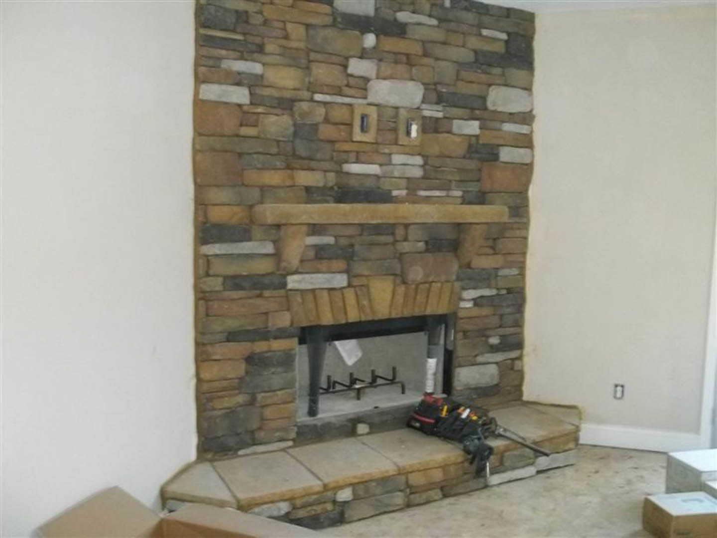 Stone fireplace with brick wall surround, wood-burning stove on hearth, built-in shelf, and hardwood floor in indoor living space