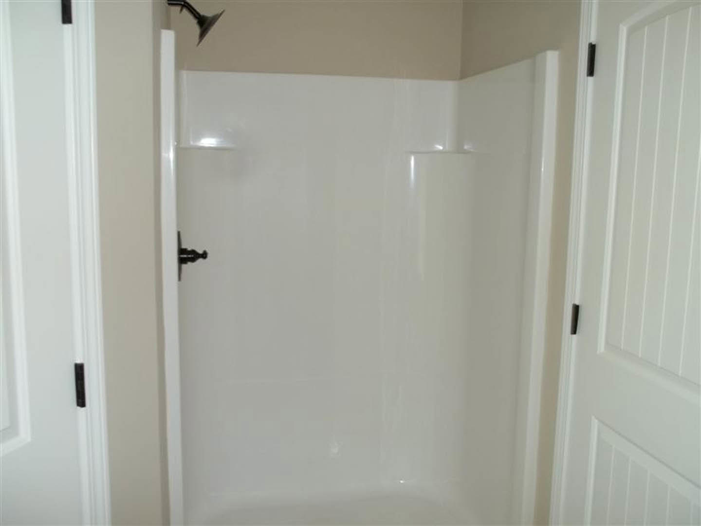 White walk-in shower with black-framed glass door, black door handle, and white plaster walls in modern bathroom