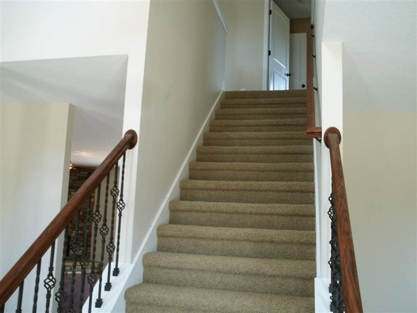 Carpeted staircase with white walls, black handrail, white door featuring a black handle, and wooden frame with metal decoration