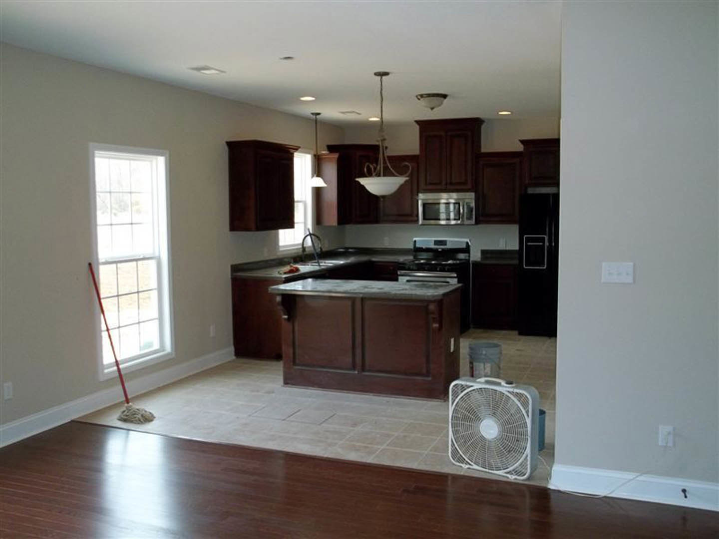 Modern kitchen with white cabinetry, stainless steel sink, dark countertop, floor fan, mop, and microwave; rope hanging from ceiling and white rectangular object with black text