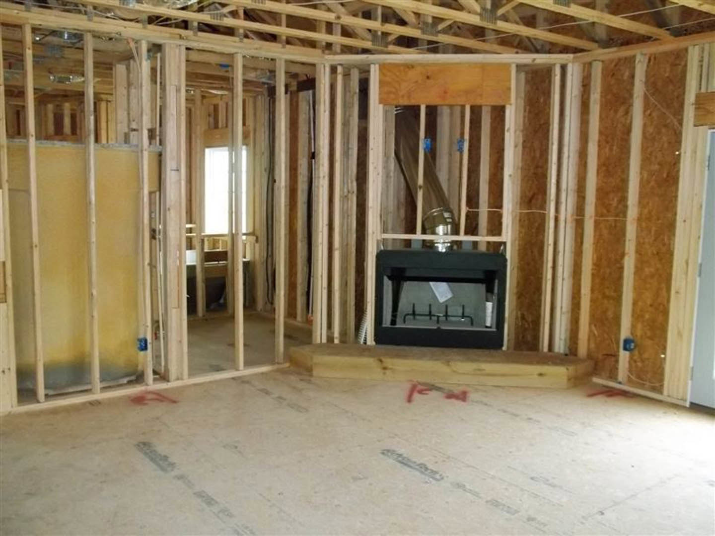 Living room with black fireplace, white painted walls, hardwood flooring, exposed wooden ceiling beams, and a gray table in the foreground.