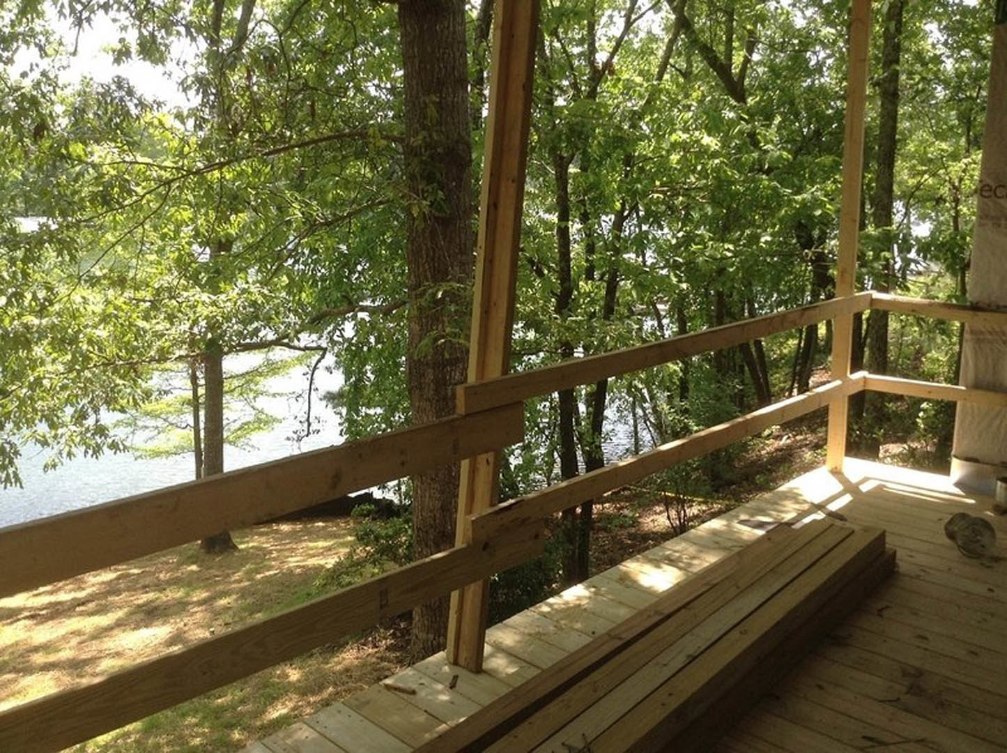 Wood deck with horizontal railing overlooking leafy trees and a lake in the background