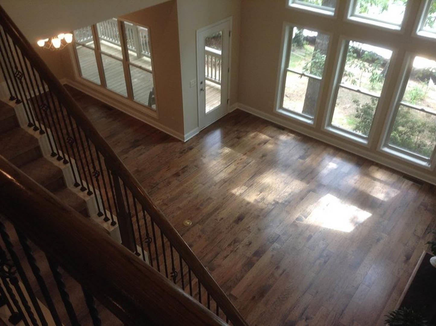 Top-down view of staircase with wooden handrails, white door, glass door, multiple windows, hardwood flooring, and string lights hanging in the room.