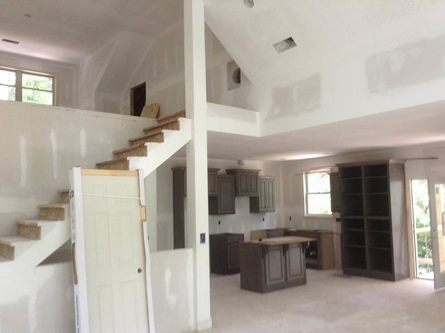 Open living space featuring wood staircase with metal railing, built-in white cabinets, corner shelving, white door with storage box, desk area, large window overlooking leafy