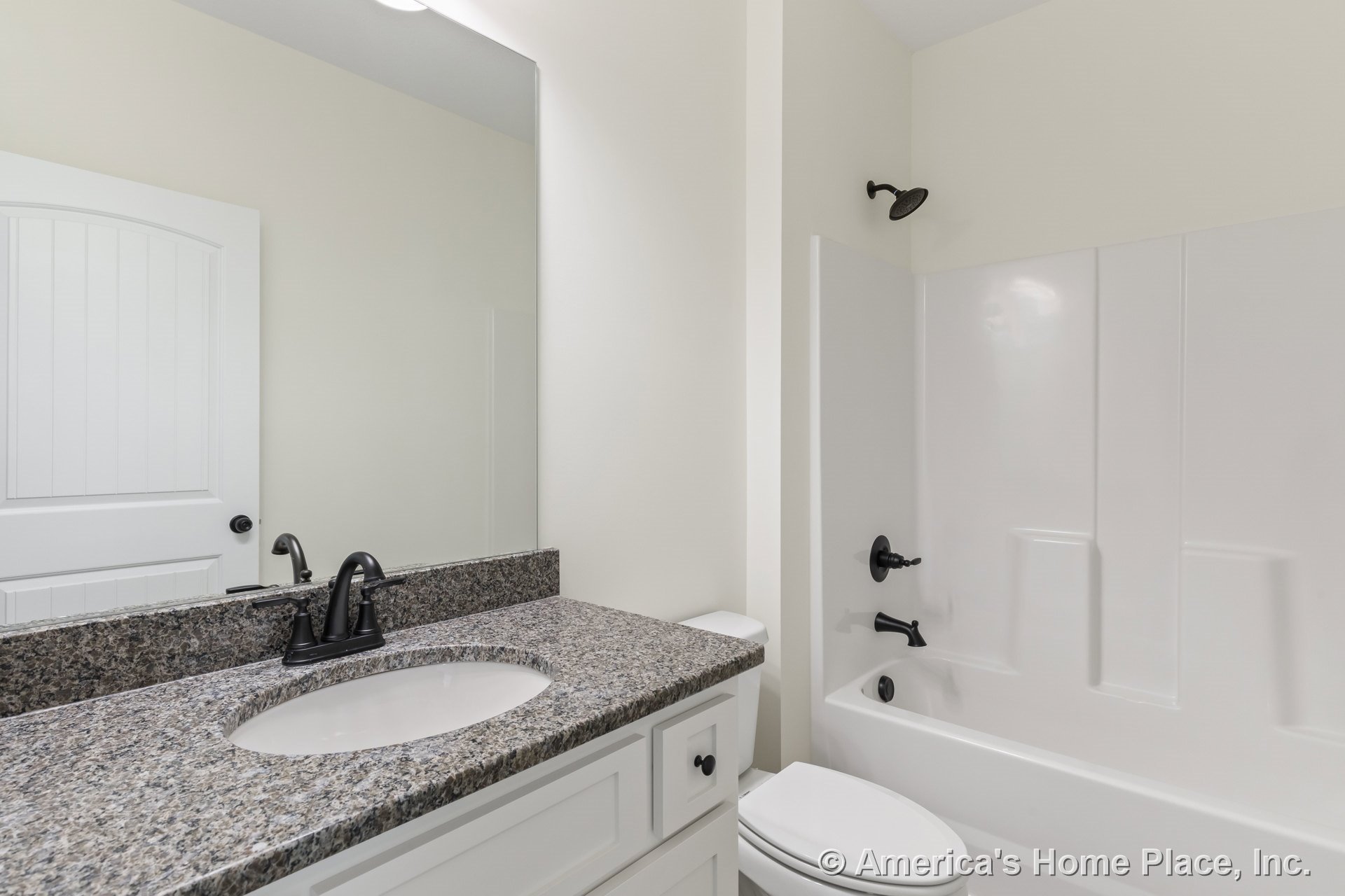 Granite countertop vanity with white shaker cabinets, large wall mirror, black faucet and hardware, bathtub with integrated surround, single sink, white paneled door, neutral