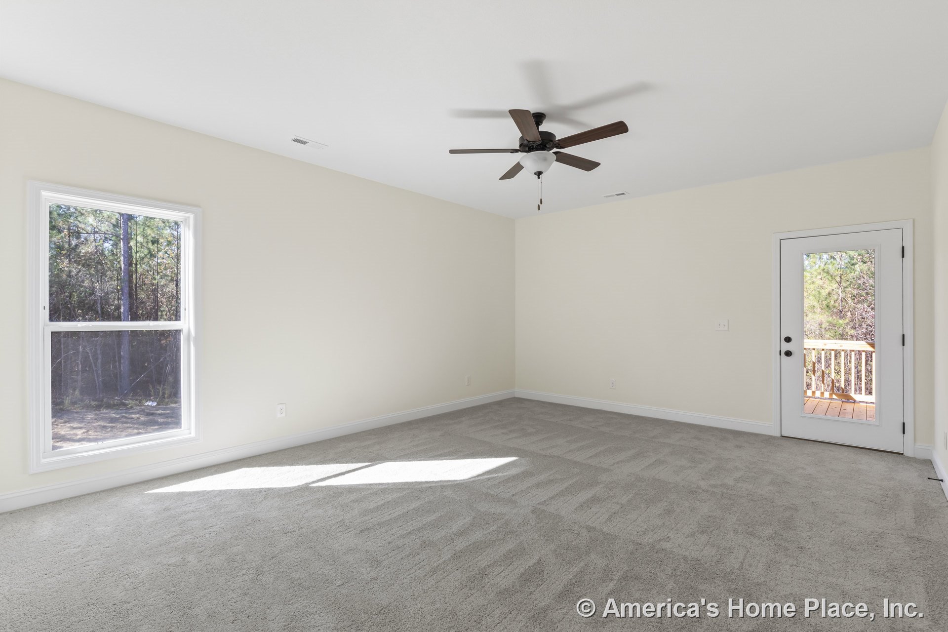 Spacious bedroom with wall-to-wall carpet, neutral walls, large double-hung window, glass exterior door opening to a wooden deck, ceiling fan with light, baseboard trim, and