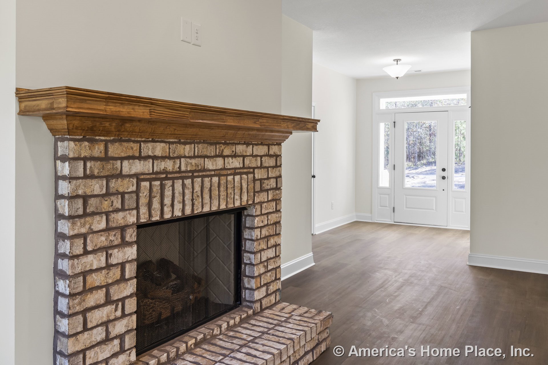 Brick fireplace with wood mantel in living area adjacent to entryway featuring double doors with sidelights and transom window, hardwood flooring, white trim and baseboards, and