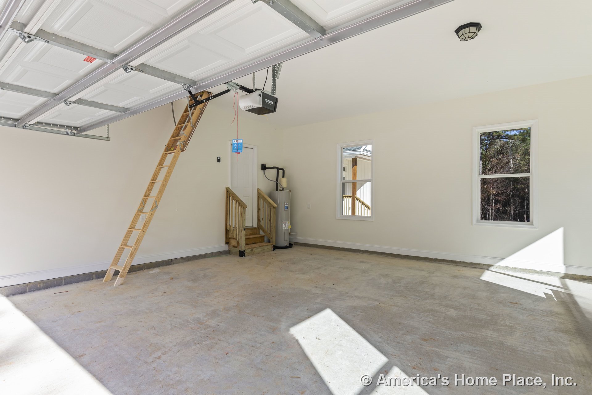 Pull-down attic ladder in garage with unfinished concrete floor, two double-hung windows, ceiling-mounted light fixture, water heater positioned beside small stairway, and white