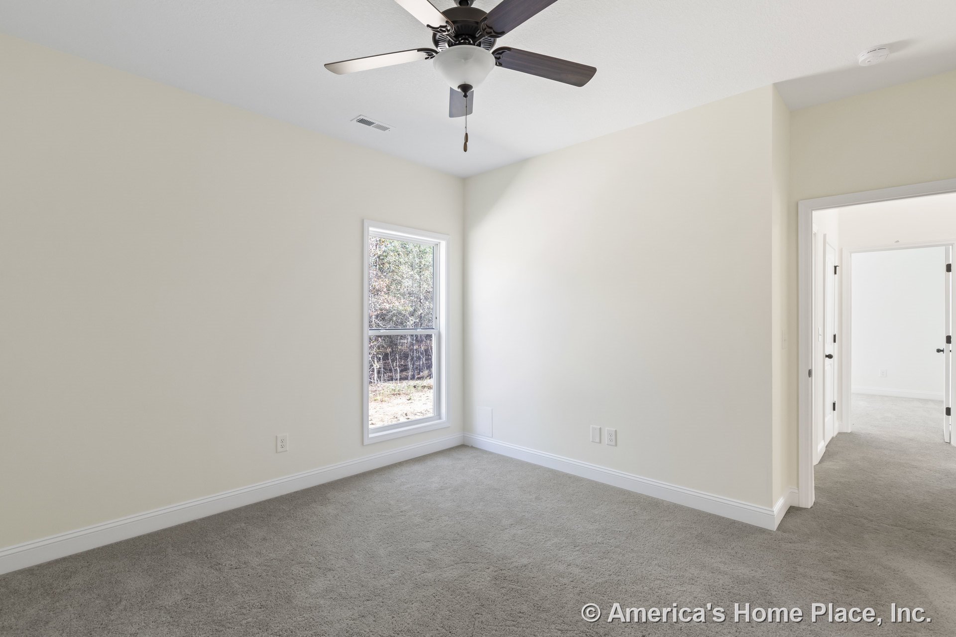 Bedroom with light carpet flooring, neutral walls, white trim and baseboards, large window allowing natural light, ceiling fan with integrated light fixture, and doorway leading to