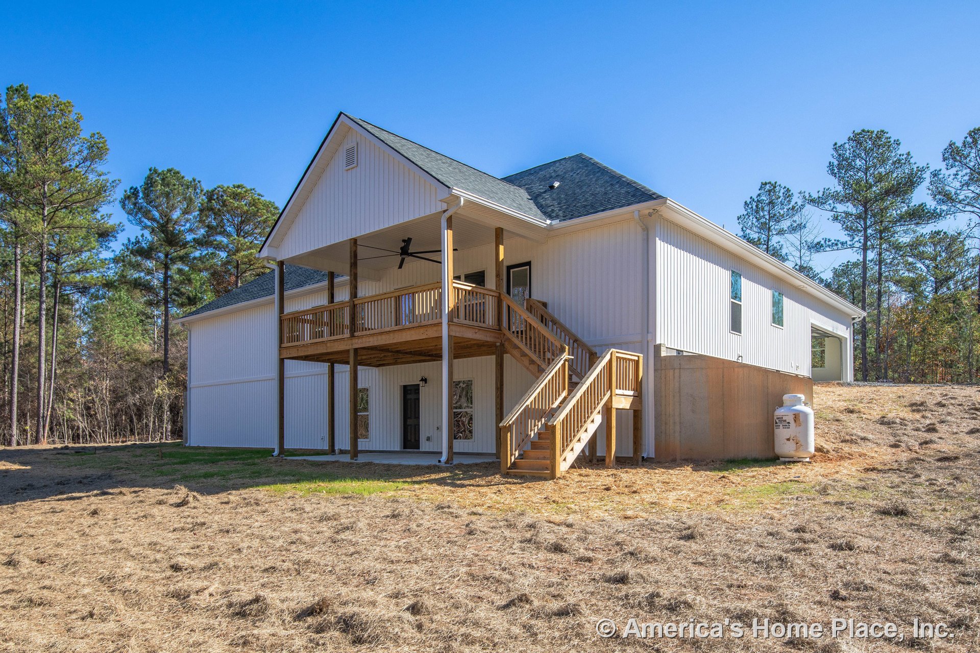 Two-story covered porch with wood railings and stairs, vertical white siding, dark shingle roof, lower patio area, large ceiling fan, multiple windows and doors with white trim.