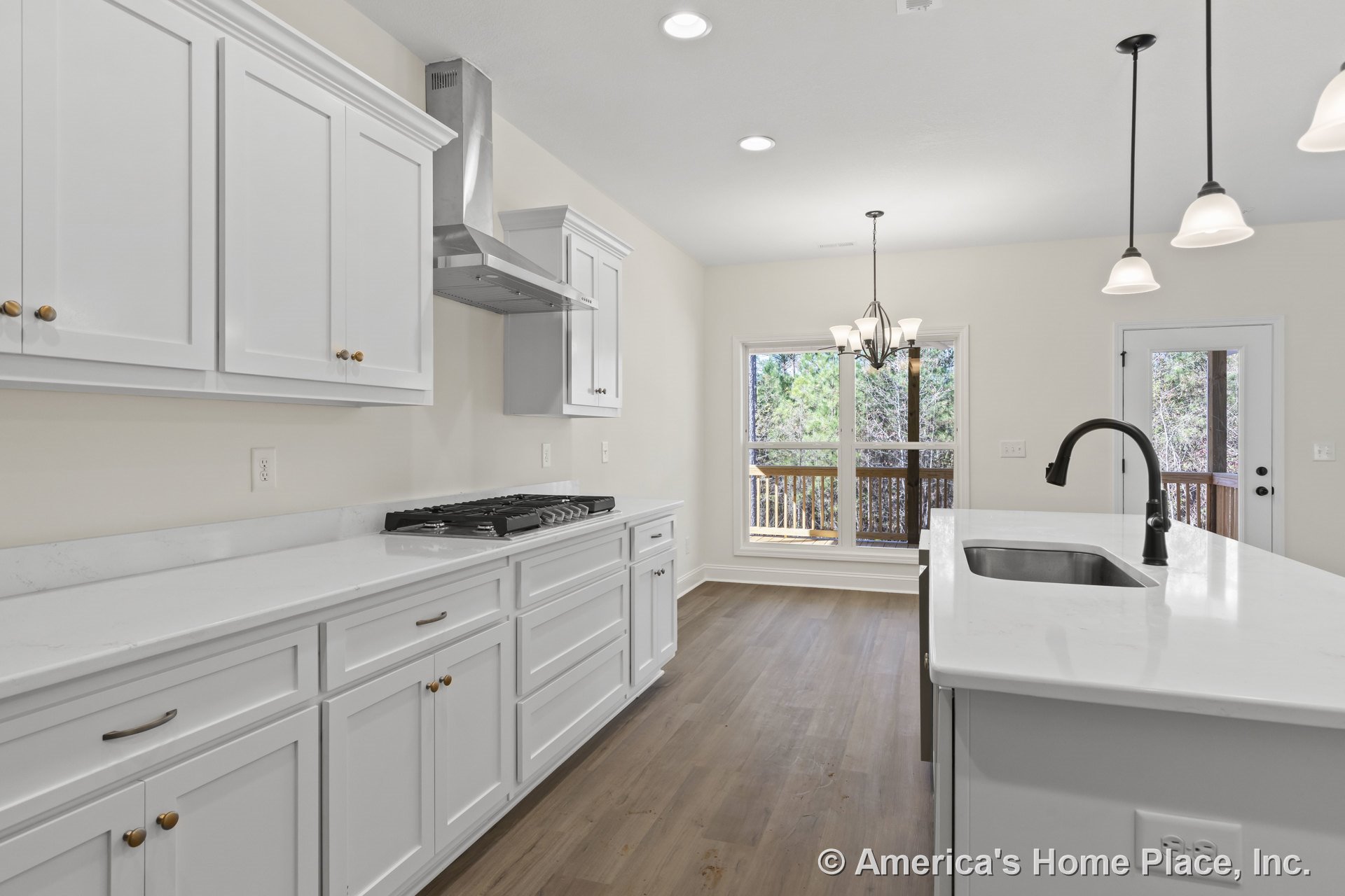 White shaker cabinets and quartz countertops with stainless steel range hood and gas cooktop, pendant and chandelier lighting, large windows overlooking backyard, hardwood