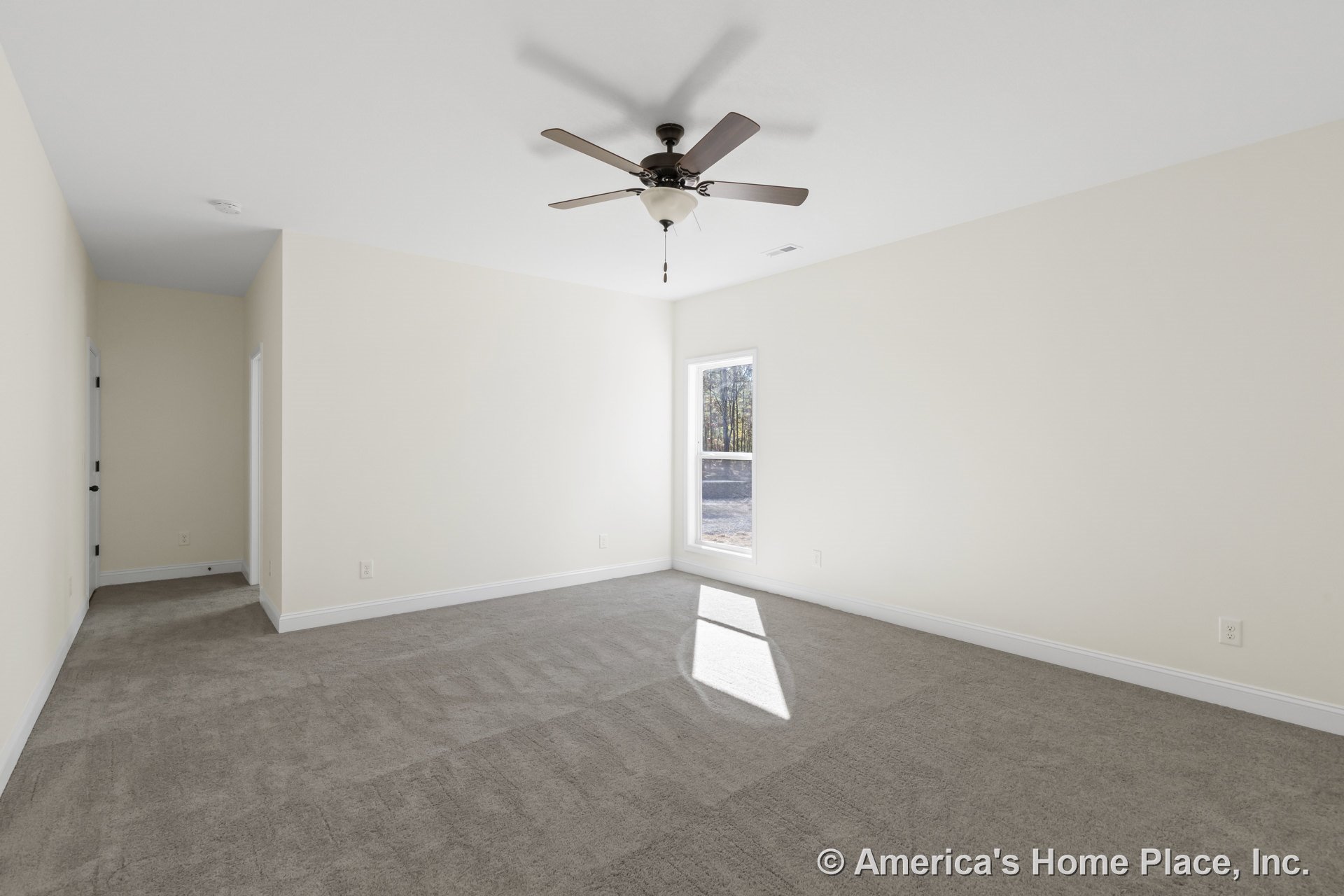 Beige carpet flooring, ceiling fan with integrated light fixture, large window with white trim, neutral wall color, white baseboards, doorway leading to adjacent room.