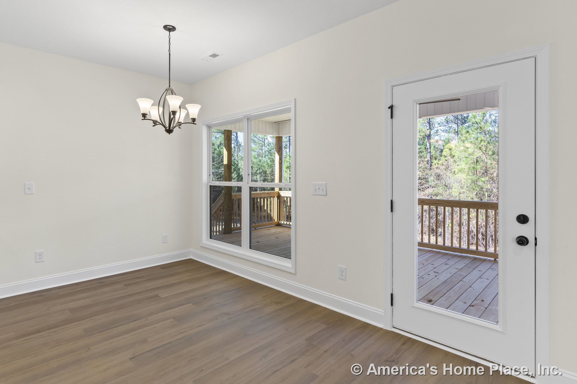 Dining area with modern chandelier, light wood flooring, large double windows, glass exterior door, white trim and baseboards, leading to covered wooden porch.