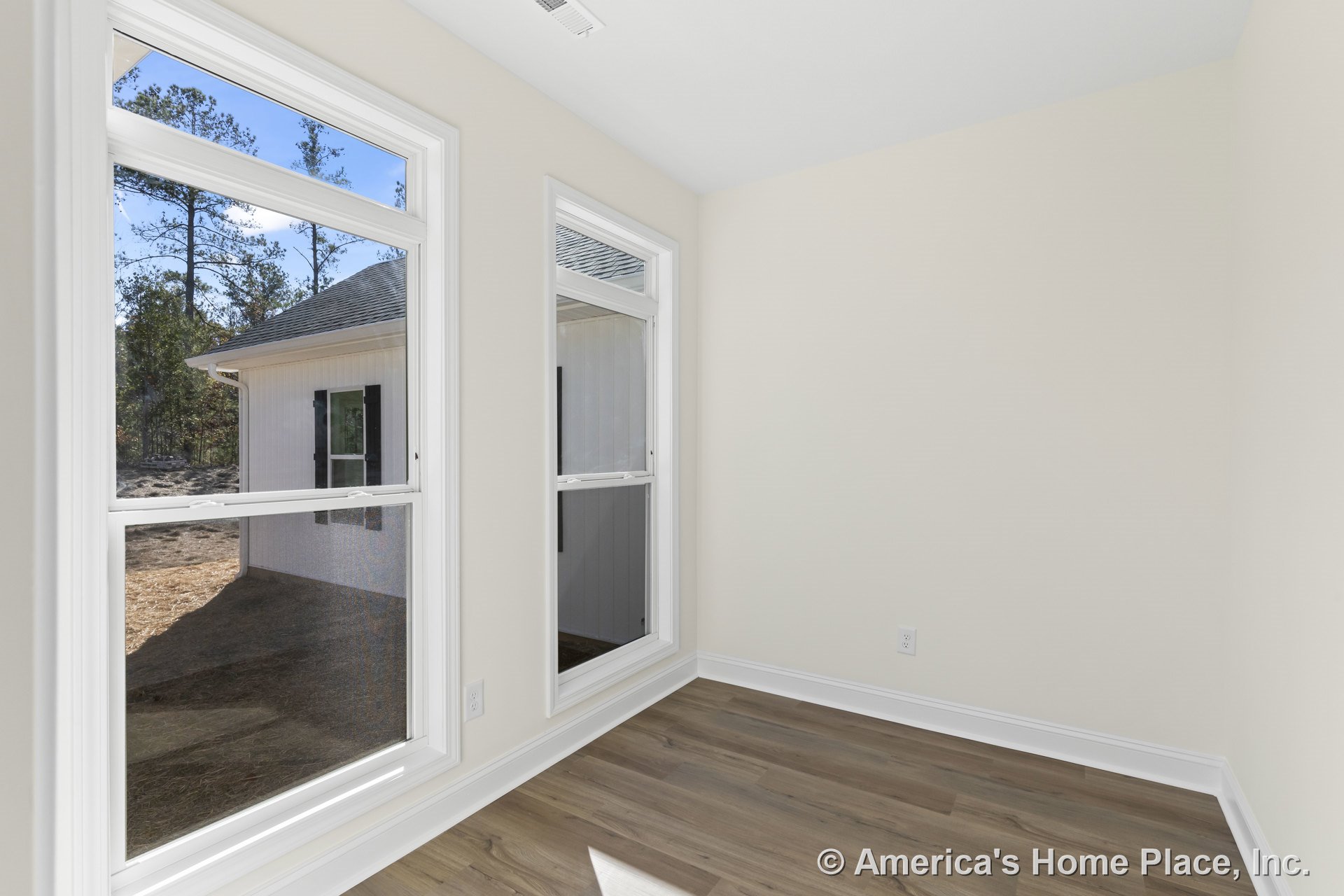 Two large double-hung windows with white trim allow natural light into a small room with light wood flooring, neutral wall color, baseboard molding, and a ceiling vent.