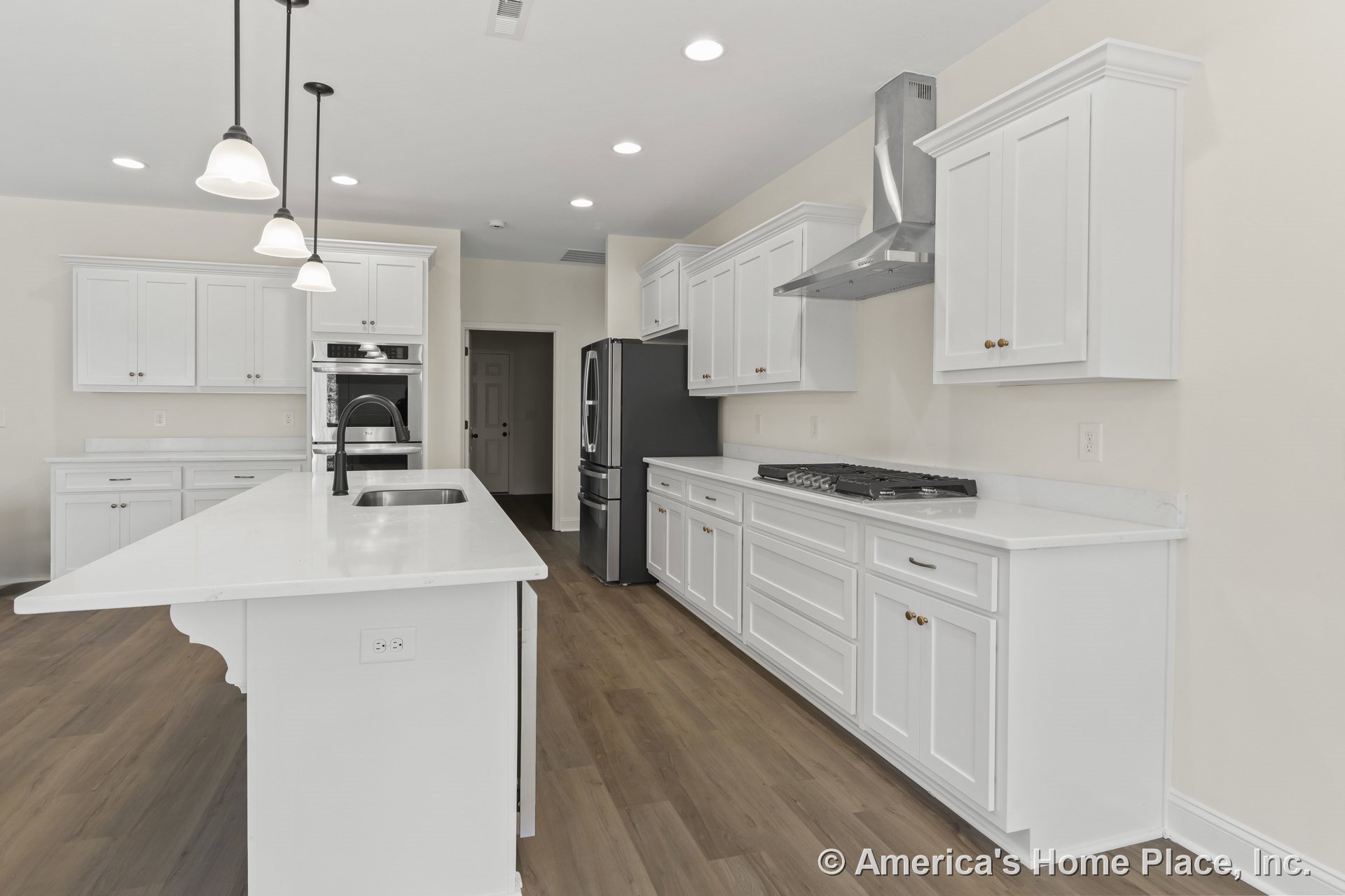 White shaker cabinetry and quartz countertops in a spacious kitchen with a large island featuring a built-in sink, pendant lighting, wood-look flooring, stainless steel appliances