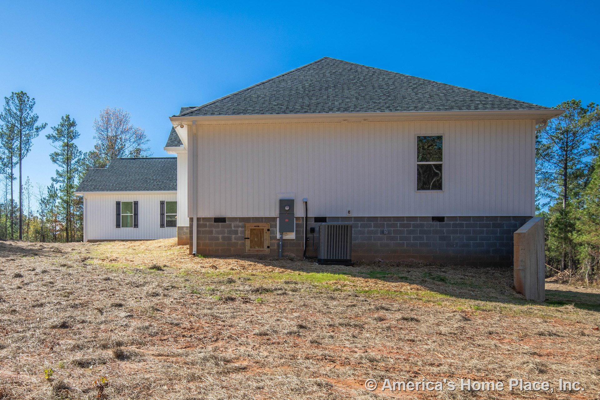 White vertical siding exterior with gray shingle roof, concrete block foundation, single window framed with trim, exterior HVAC unit, and utility meter panel.