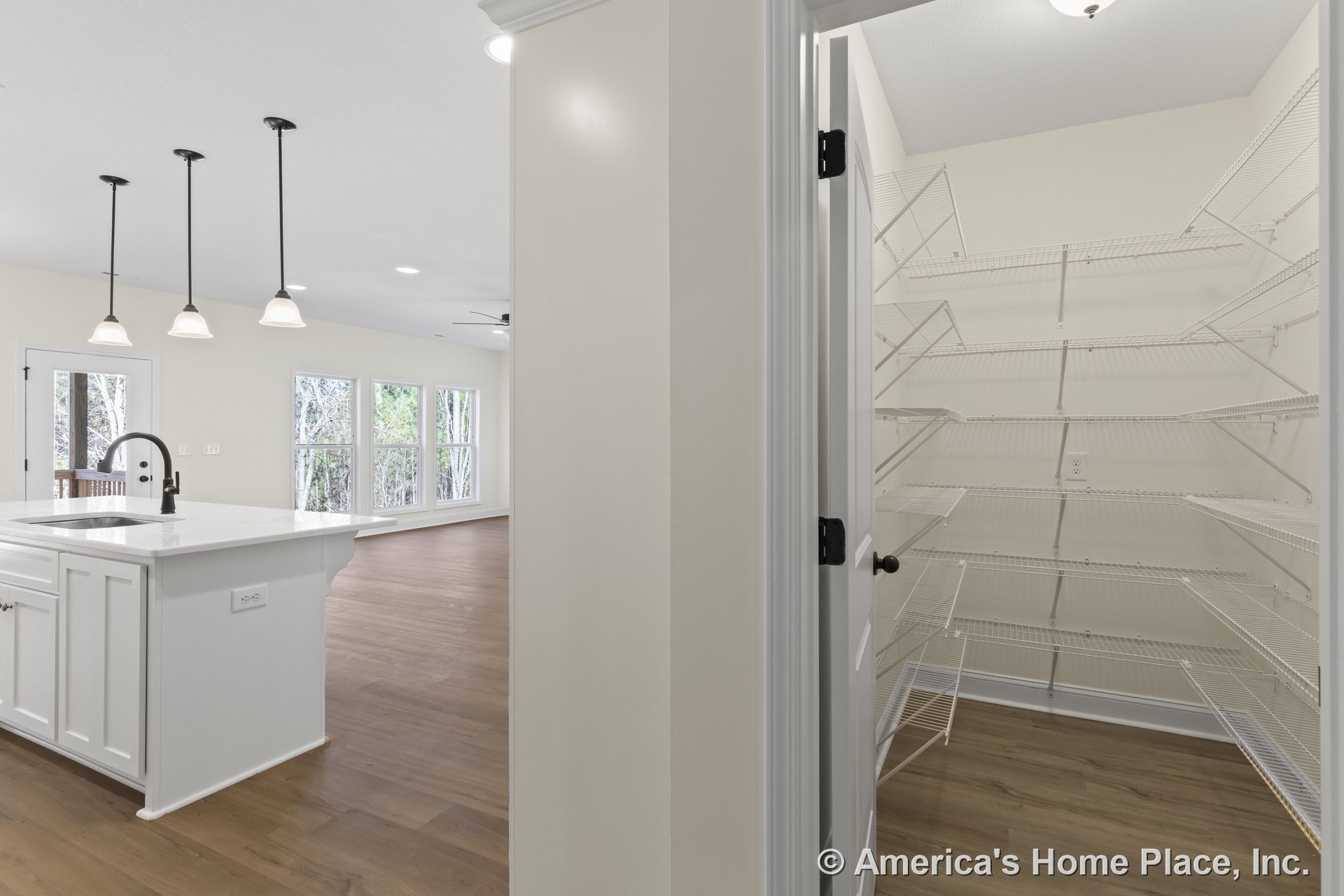 White kitchen cabinetry and marble countertop island with black faucet, pendant lights above, walk-in pantry with wire shelving, open floor plan with wood flooring, recessed