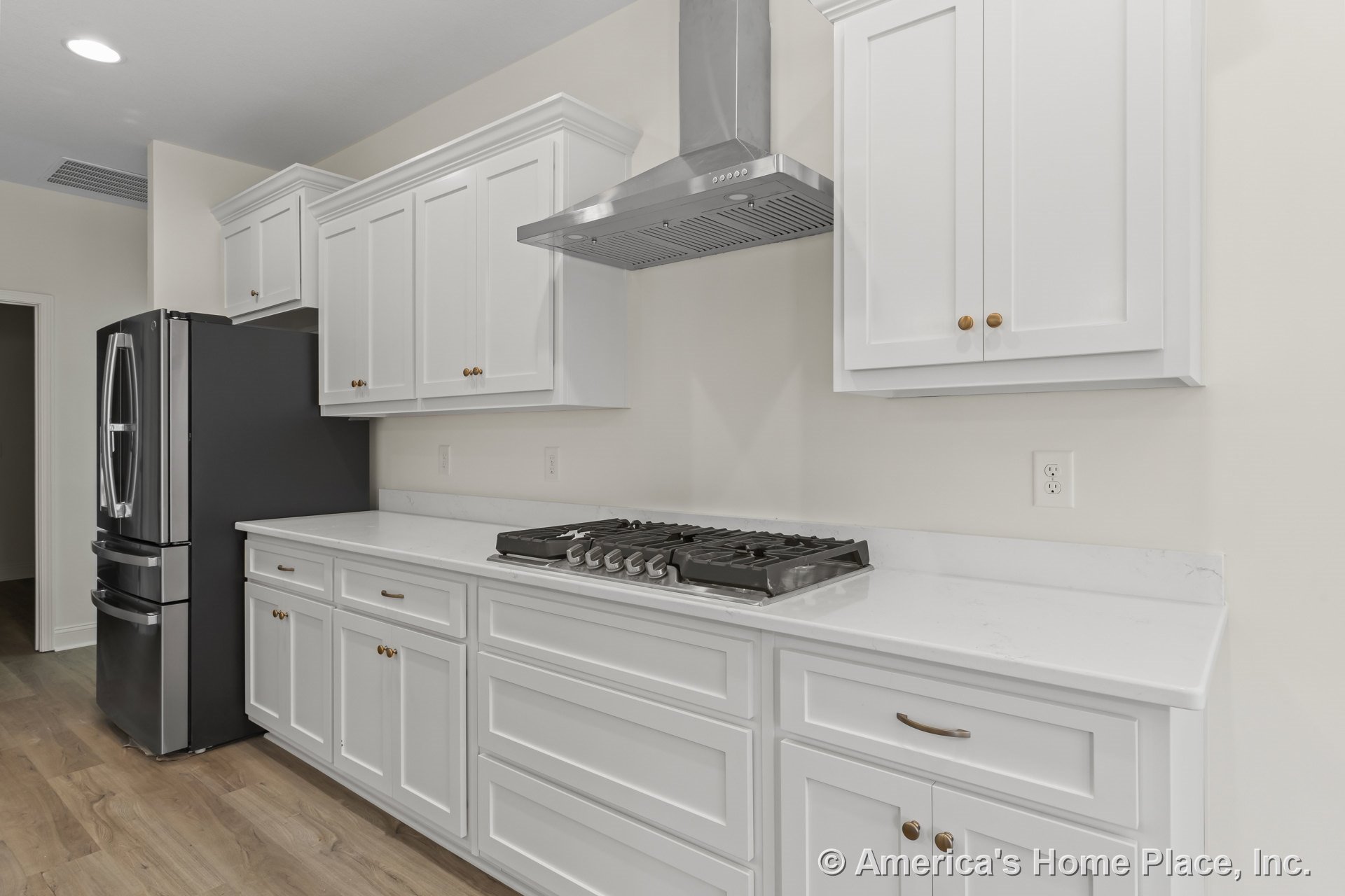 White shaker upper and lower cabinets with brushed hardware, marble-look quartz countertops, stainless steel gas cooktop and matching vent hood, modern refrigerator, wood plank