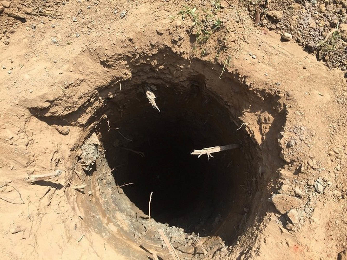 Freshly dug hole in compacted soil surrounded by loose dirt, outdoor construction site for residential foundation