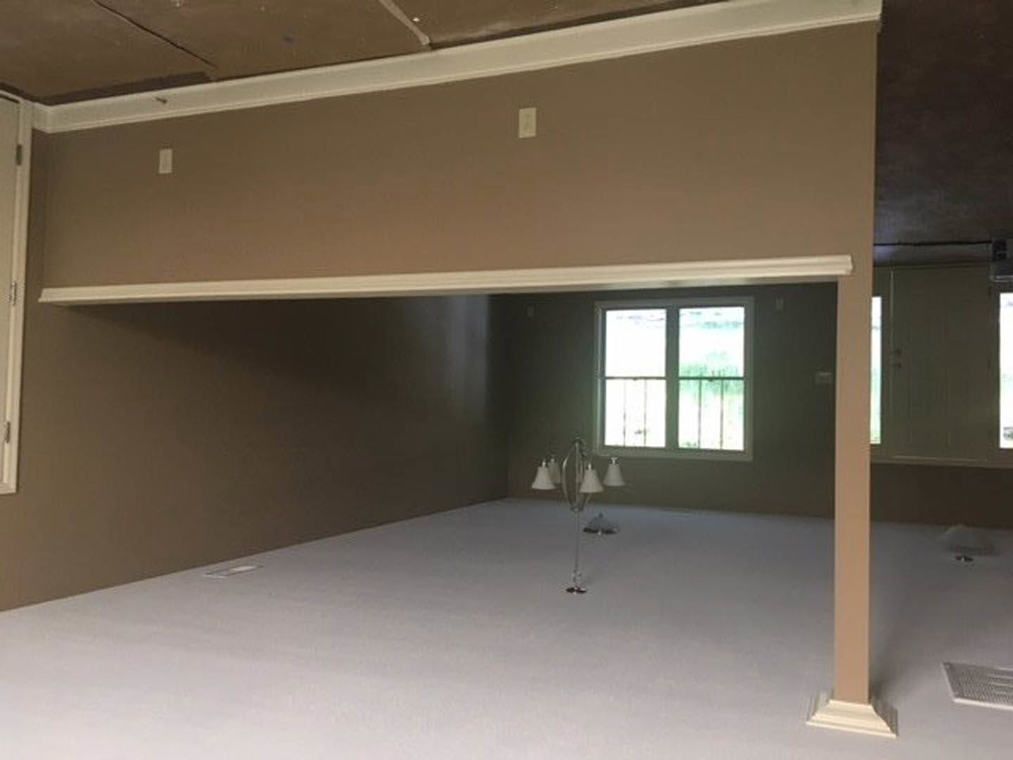 White floor room with plaster walls, large window framed by metal bars, floor lamp with white shades, ceiling beam, and visible vent.