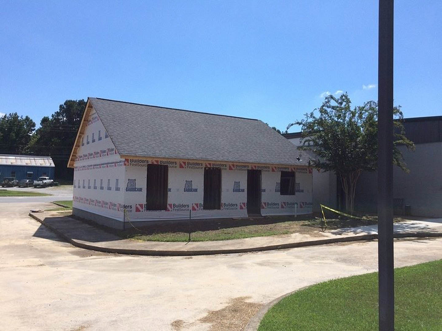 Modern custom home exterior with white siding, large windows, and a manicured lawn; temporary signs posted near entry; mature tree in foreground under clear blue sky