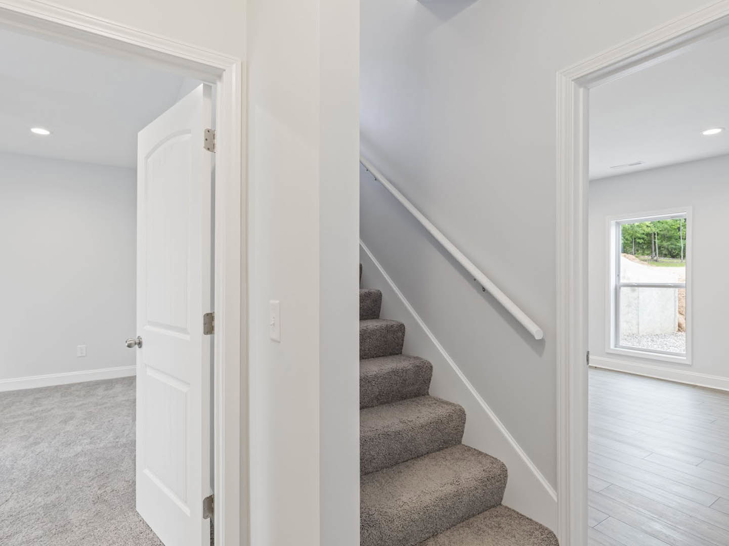 Carpeted staircase with white wood railing and white walls, large window revealing trees outside, white wood flooring at base
