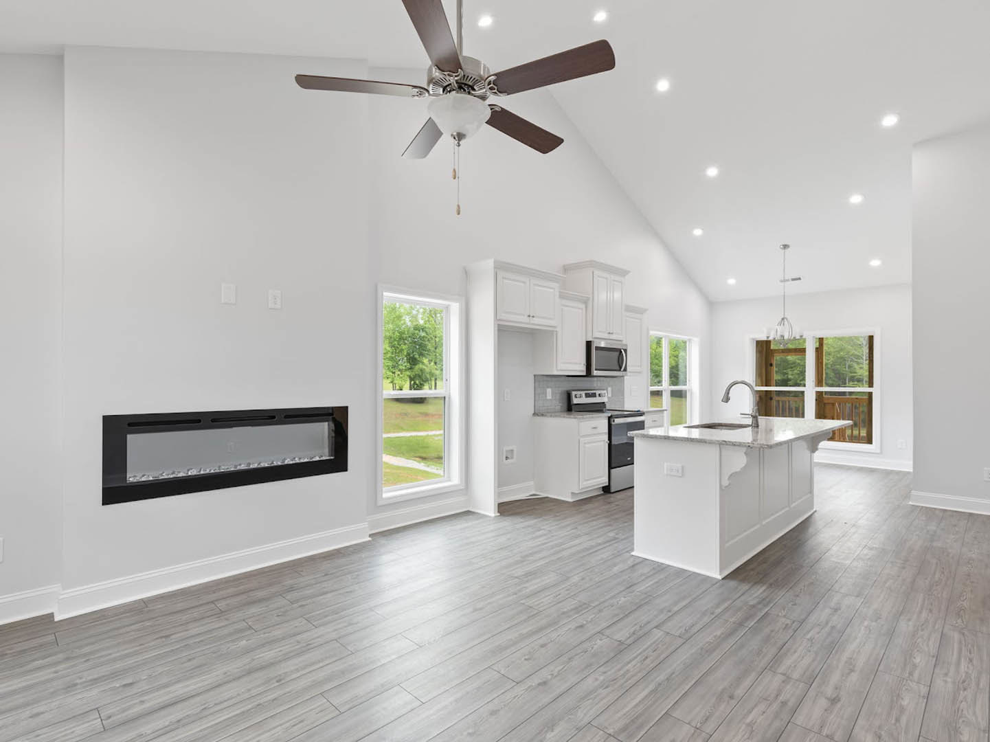 Open kitchen and living room featuring a ceiling fan with light fixture, white kitchen island with built-in sink, wood flooring, white cabinetry, stainless steel microwave, and
