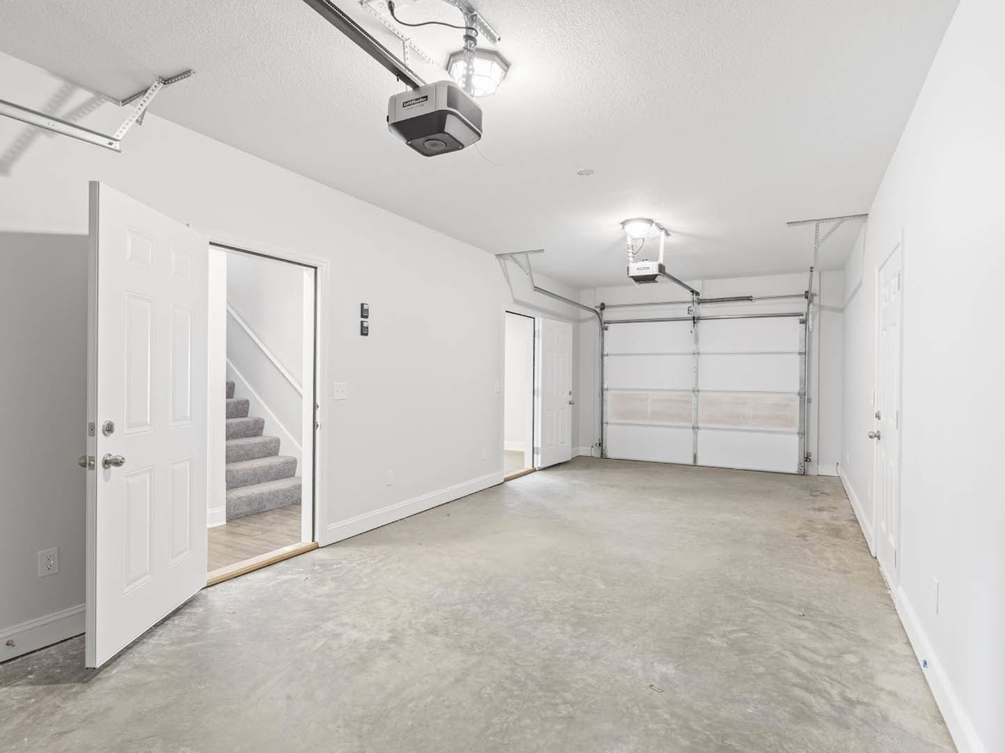 Garage interior with smooth concrete flooring, white plaster walls, open white door, and ceiling fan visible above