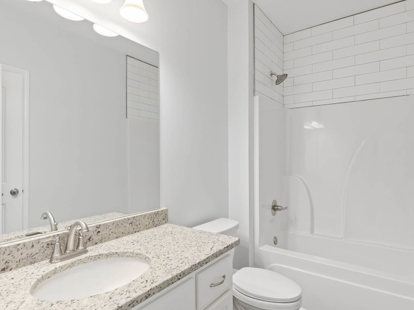 Modern bathroom with white tile walls, glass-enclosed shower, white porcelain sink and toilet, chrome faucet, and black-framed mirror