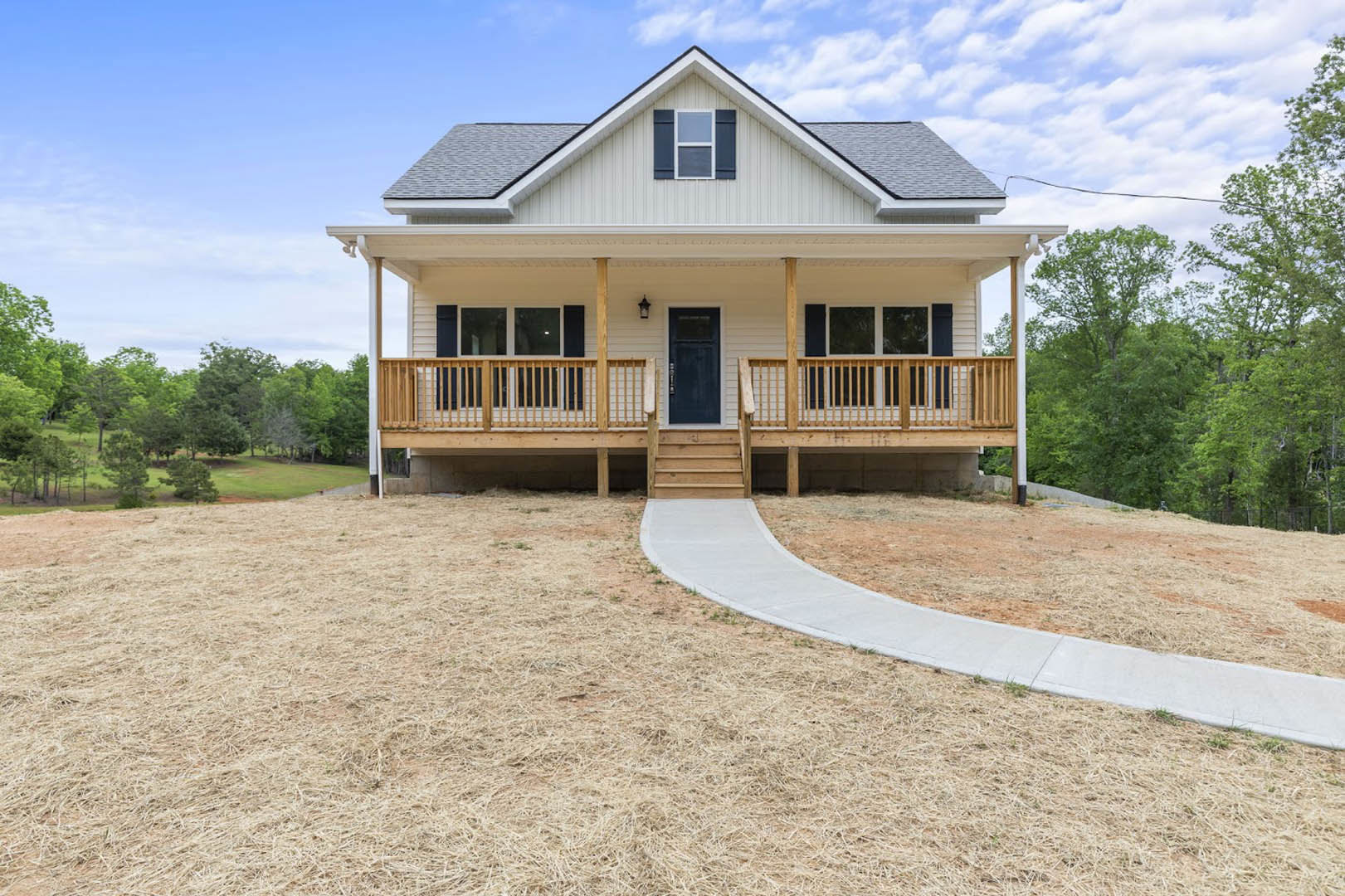 Concrete walkway bordered by grass leading to a house with a covered porch, blue front door, white trim, and multiple windows under a cloudy sky