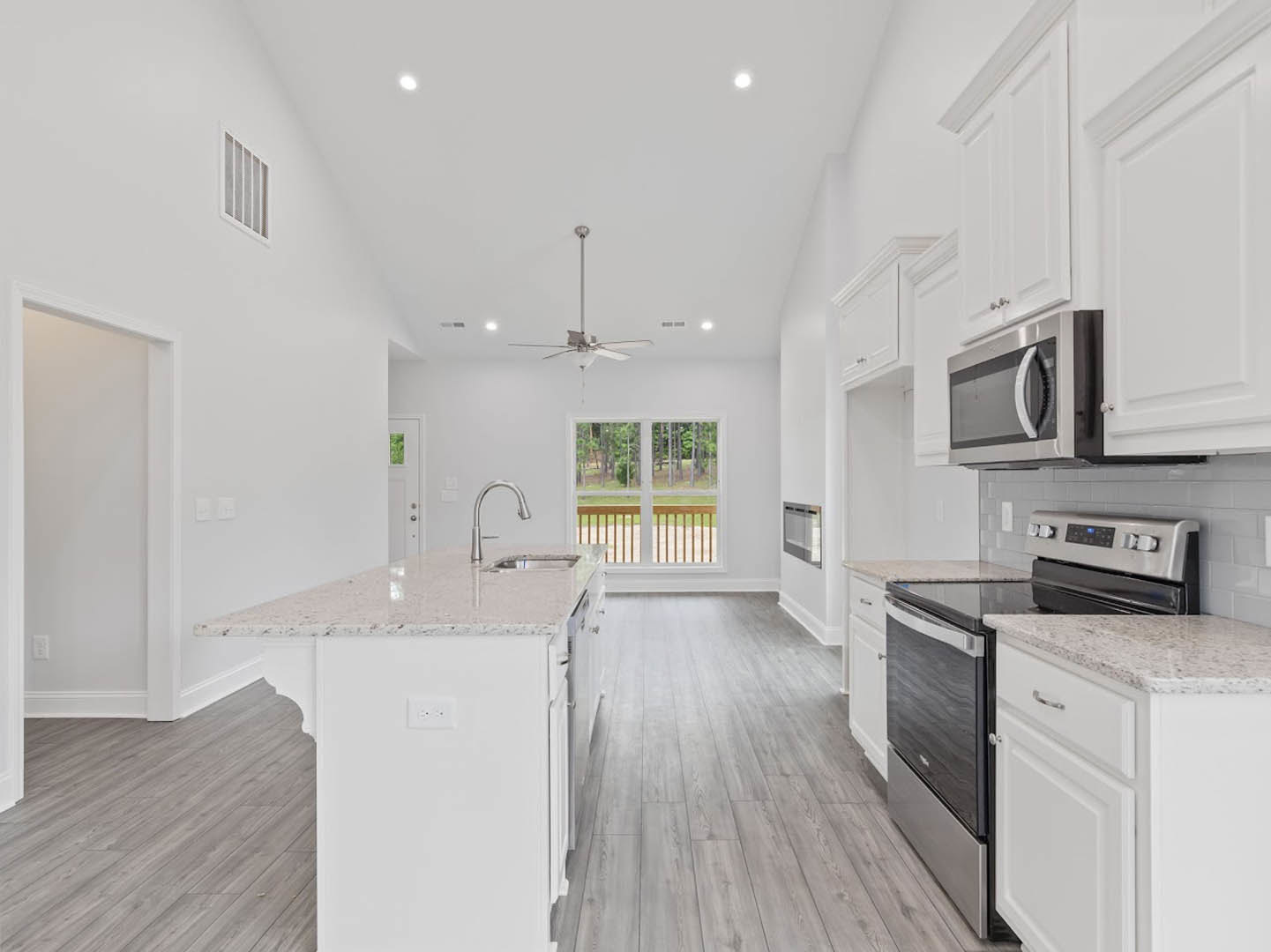Kitchen with white cabinets, white countertop island featuring a sink, wood flooring, black dishwasher, microwave oven, window overlooking trees and grass, ceiling fan with light
