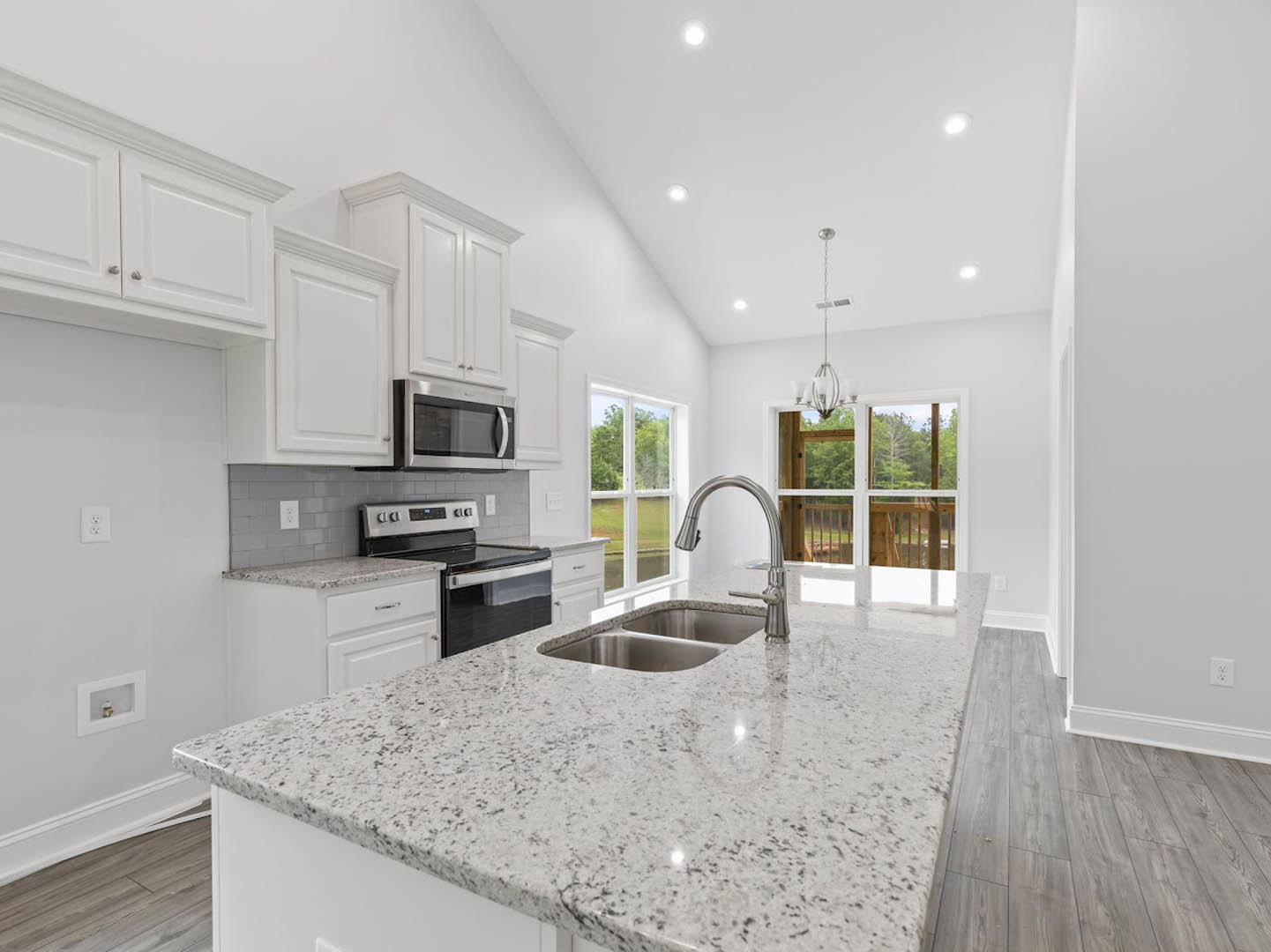Granite kitchen countertop with double stainless steel sinks, white cabinetry, built-in microwave, stove, and balcony view with trees through glass door