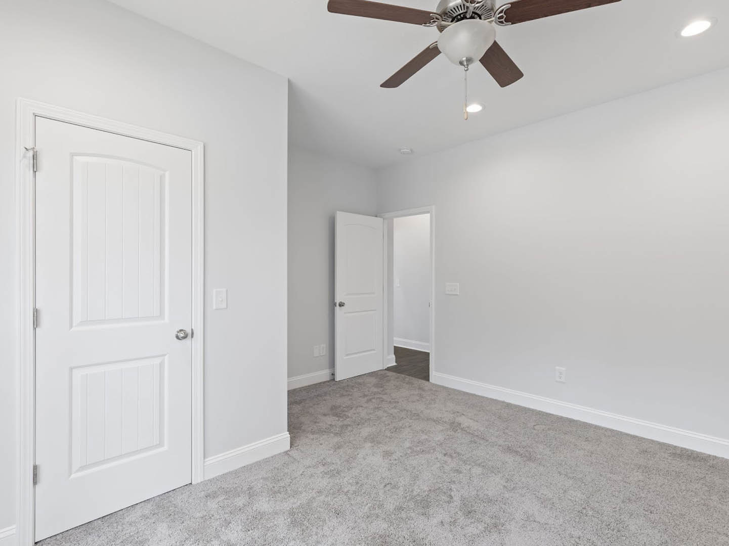 Carpeted room with white walls, ceiling fan with light fixture, and white door featuring a silver knob