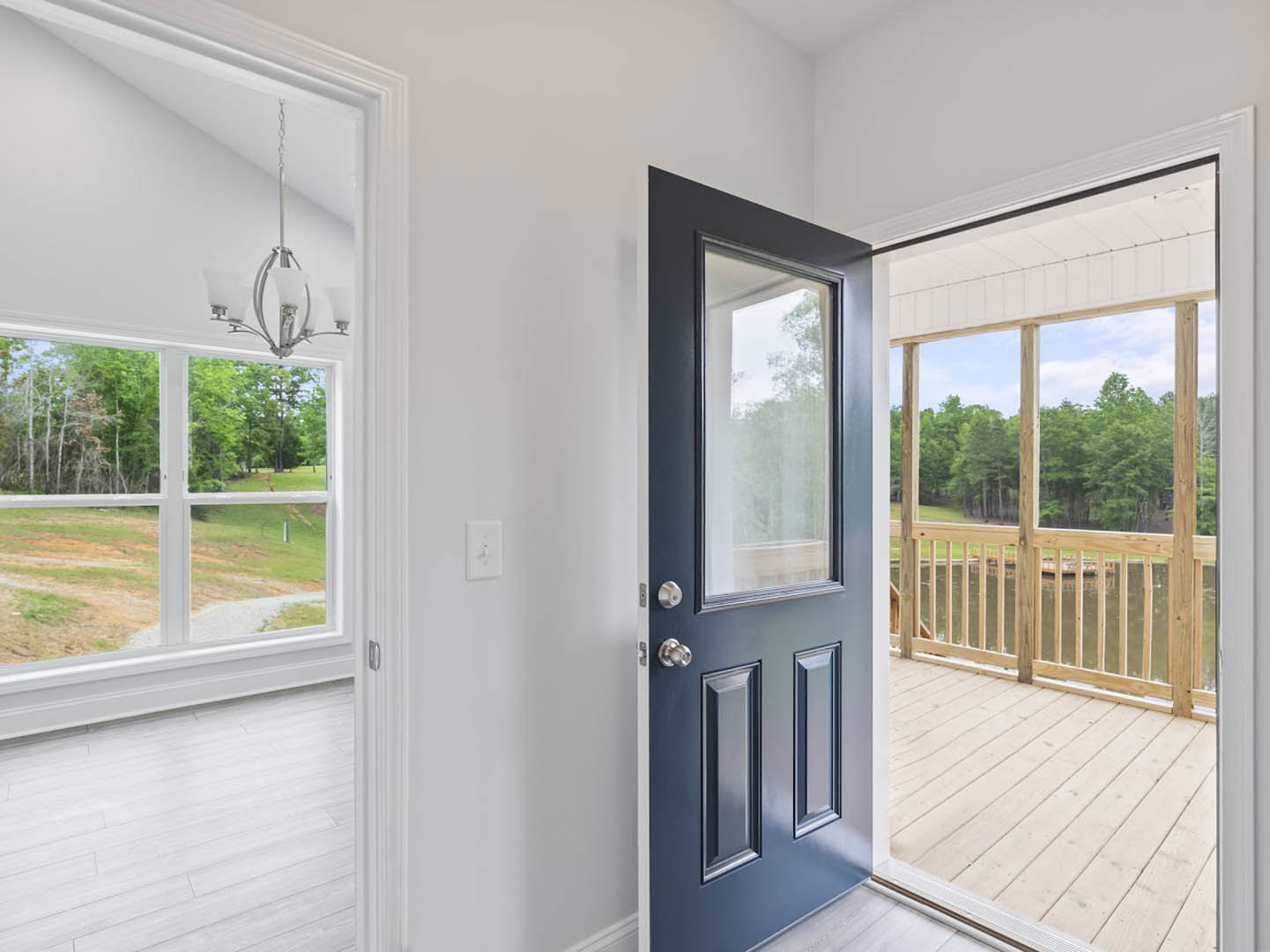 White-framed glass door opening onto a wooden deck overlooking a lake, with light switch on adjacent wall and ceiling light fixture visible inside room