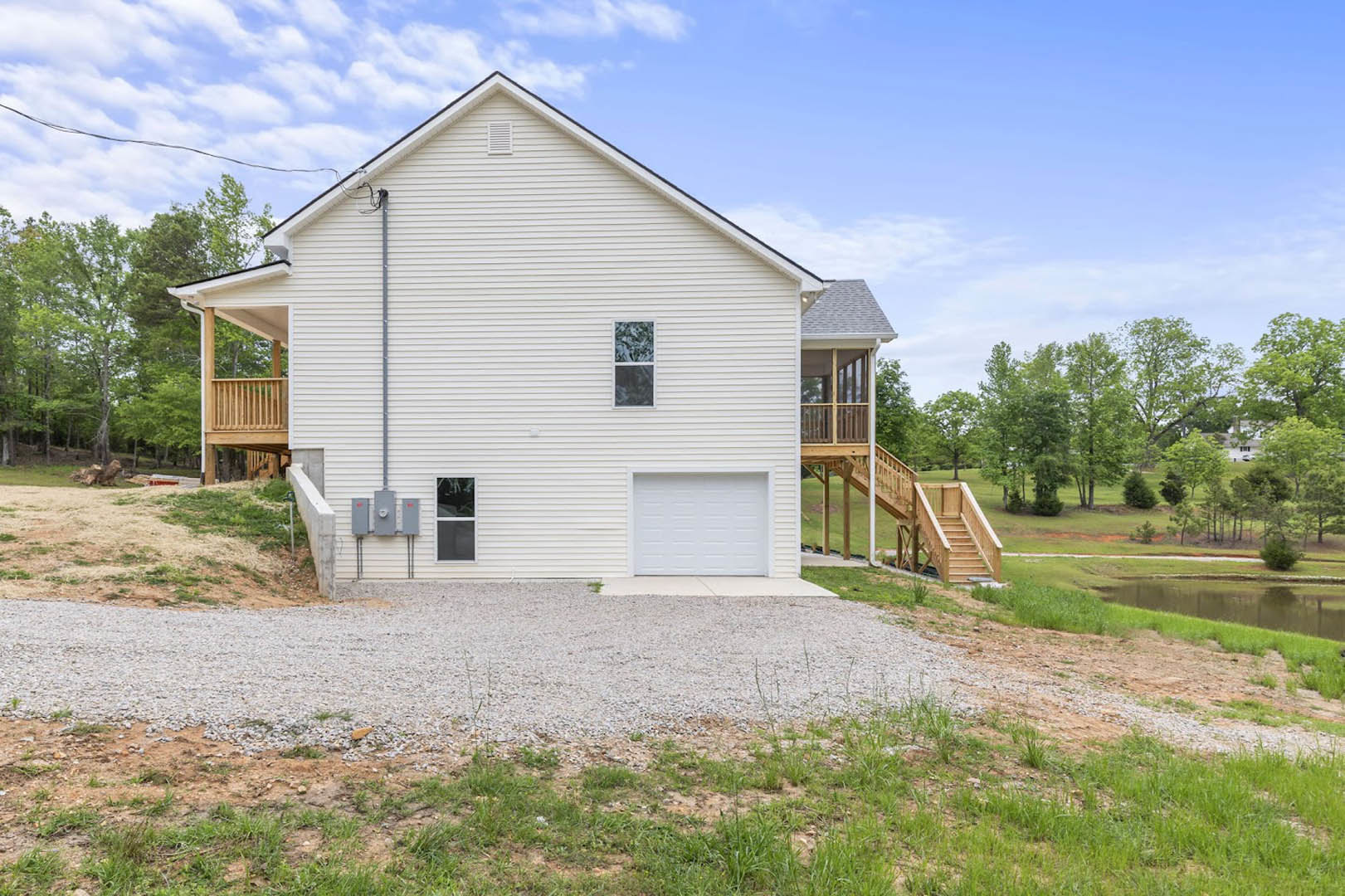 Modern home with white siding, attached garage, gravel driveway bordered by grass, and elevated wood deck with white railing.