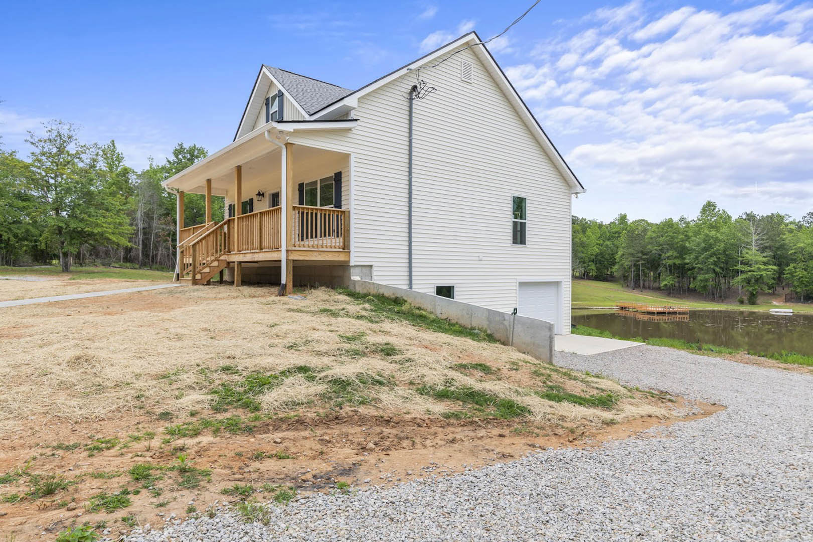 Two-story home with covered front porch, wooden deck, attached garage, paved driveway, and landscaped lawn bordered by mature trees.