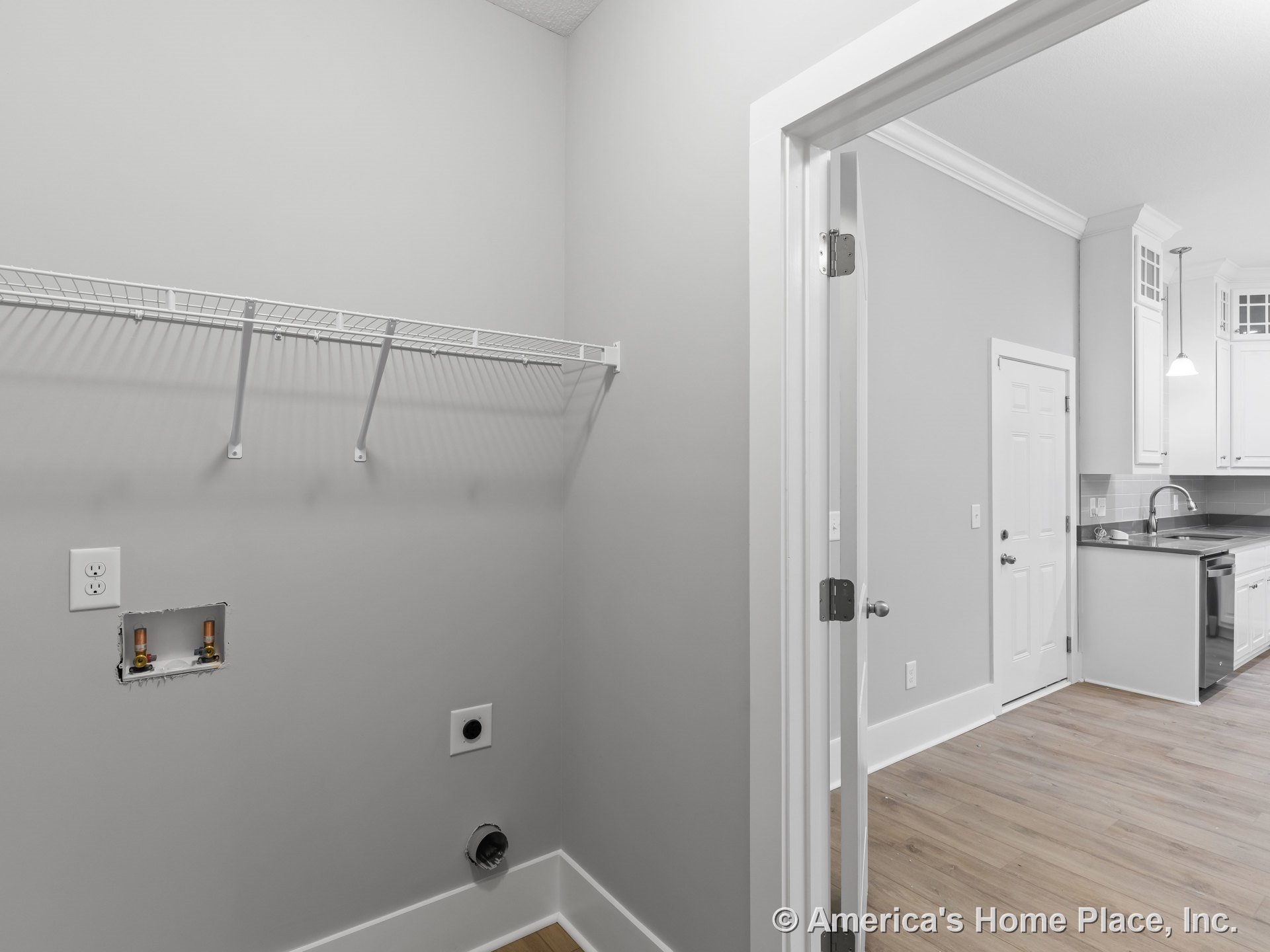 Laundry area with washer and dryer hookups, wire shelving, and white trim adjacent to kitchen featuring white cabinetry, tile backsplash, pendant lighting, stainless sink