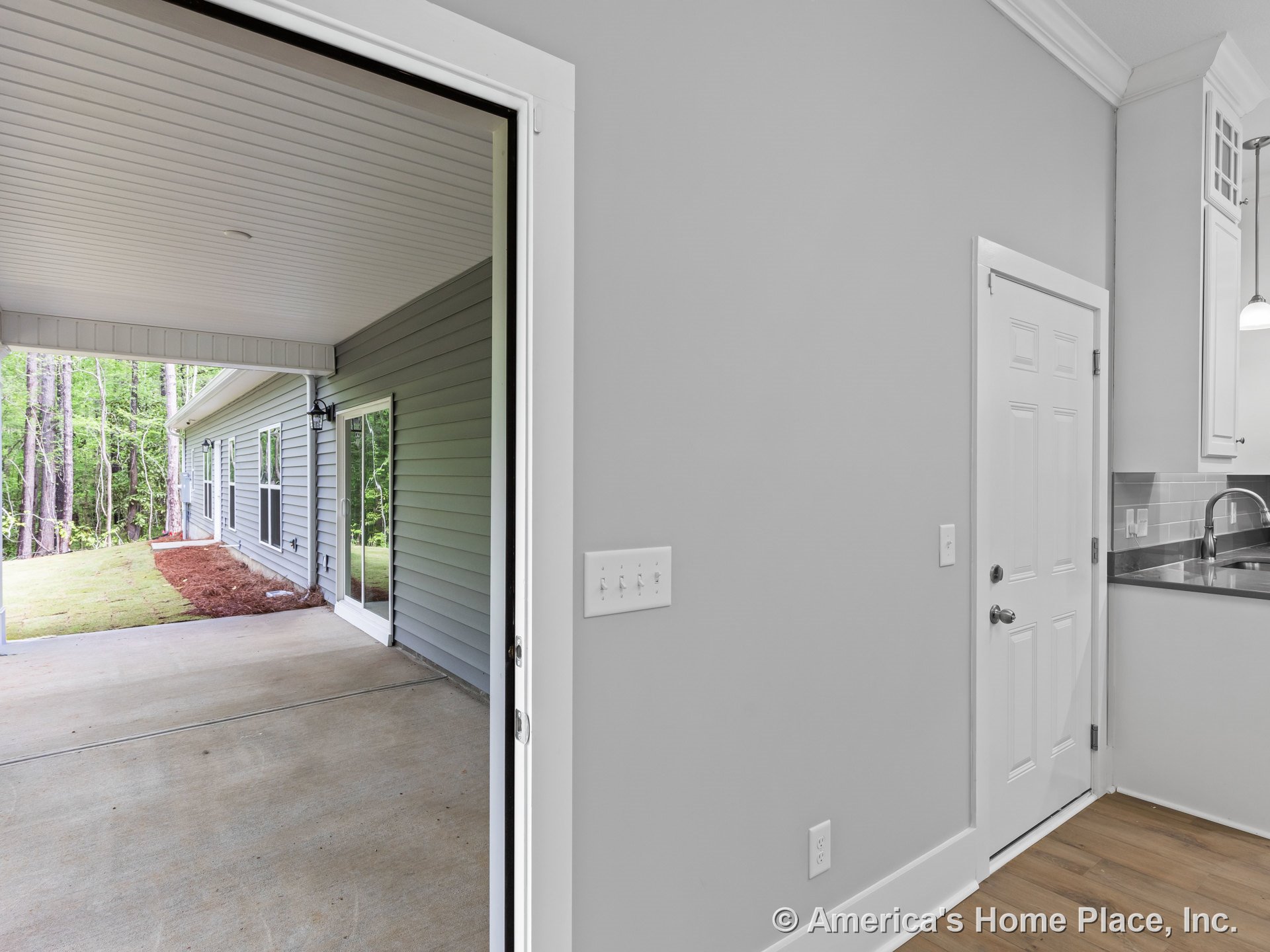 Covered patio with concrete flooring and gray exterior siding connects to kitchen featuring white cabinetry, gray countertops, tile backsplash, wood-look flooring, sliding glass