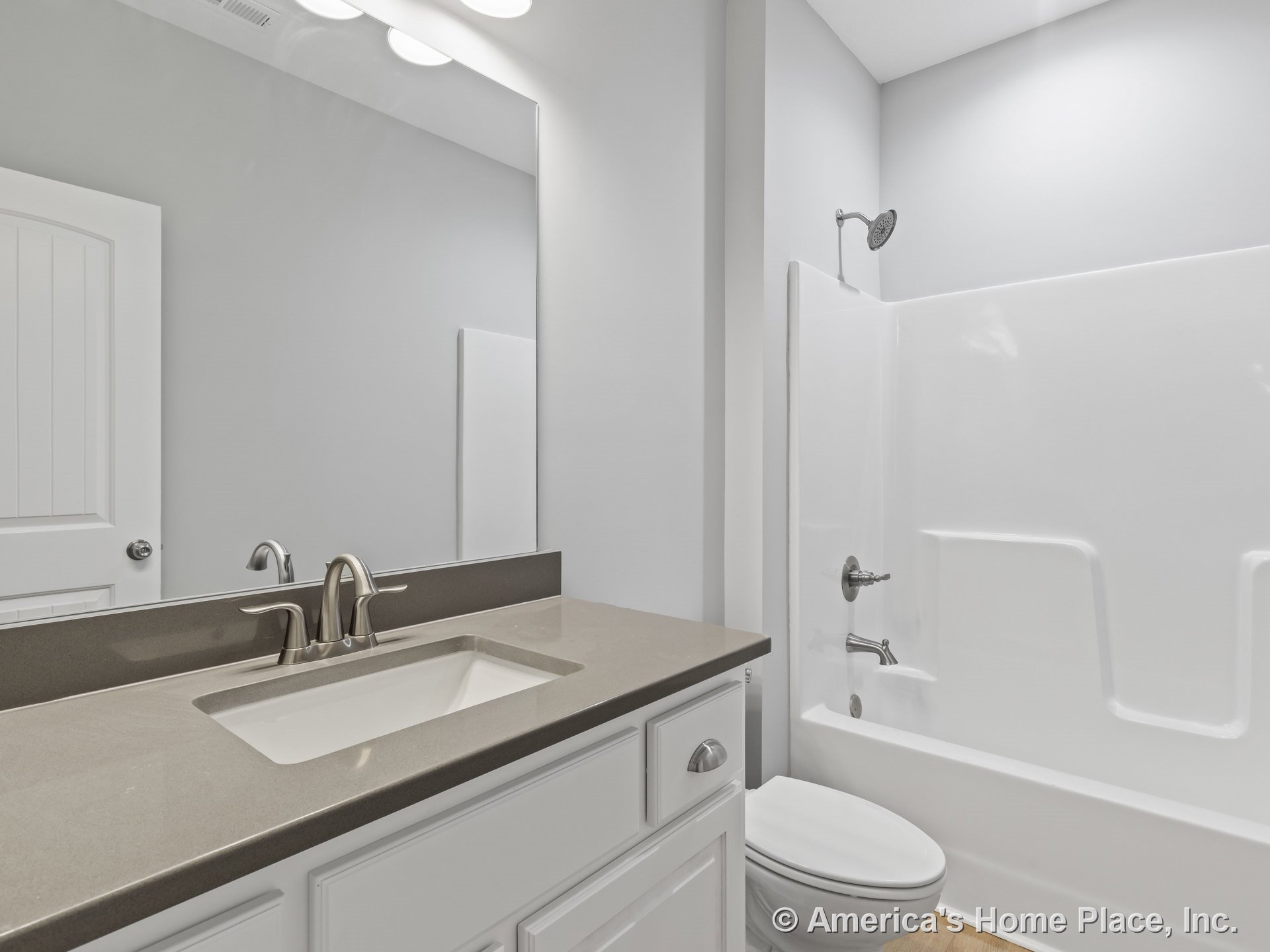 Built-in white shaker vanity with quartz countertop, brushed nickel faucet, and large wall mirror; fiberglass bathtub-shower unit with integrated surround; recessed ceiling