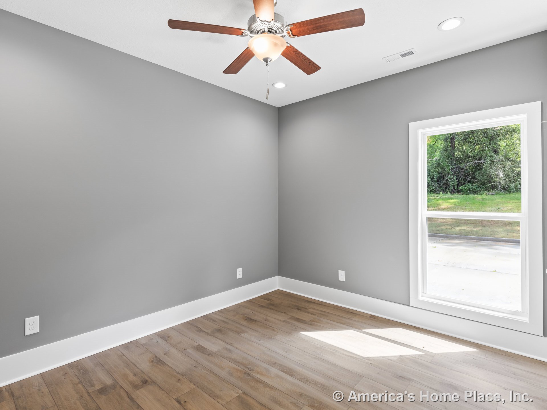 Gray walls with white baseboards and trim, wood plank flooring, large window allowing natural light, ceiling fan with integrated light fixture, and recessed ceiling lights in a