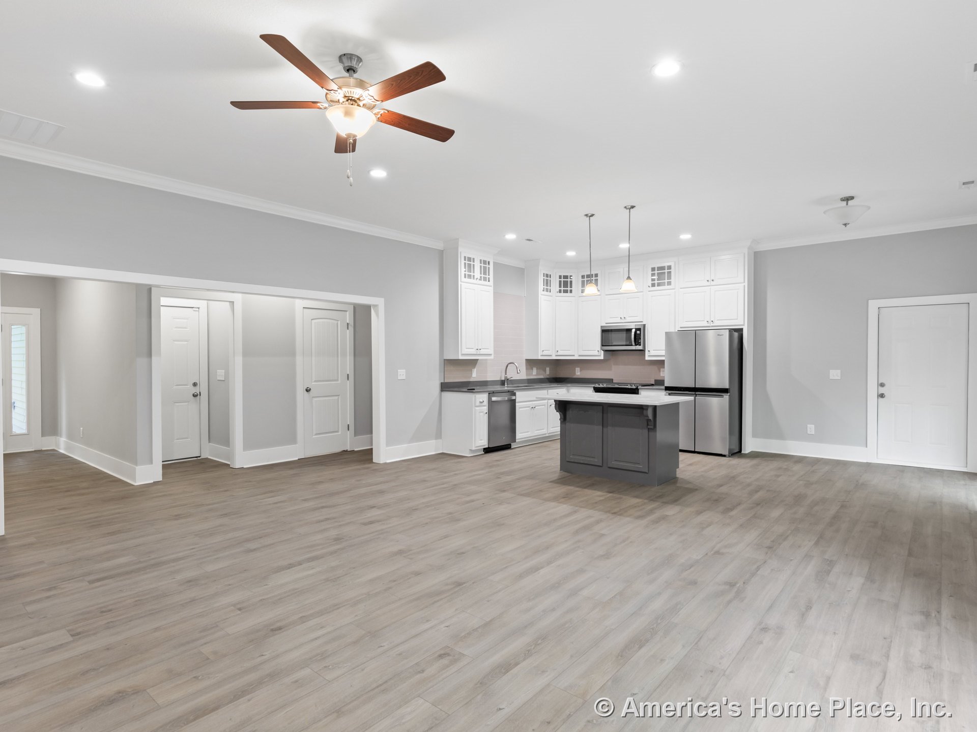 Open concept kitchen and living area with white upper cabinets, gray kitchen island, stainless steel appliances, pendant lighting, recessed lights, light wood plank flooring