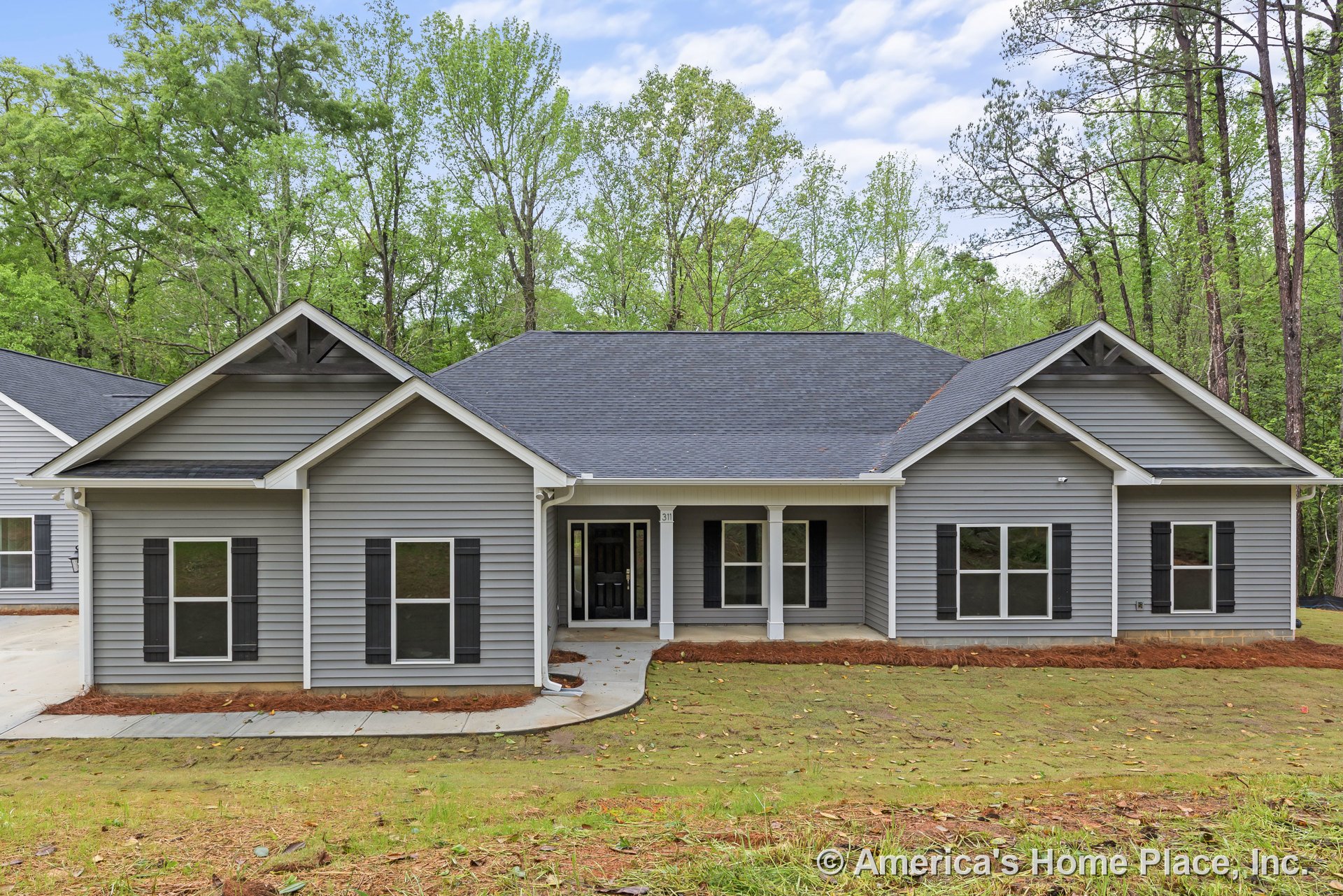 Gray vinyl siding exterior with black window shutters, covered front porch supported by white columns, asphalt shingle gabled roof, multiple double-hung windows, and paved driveway