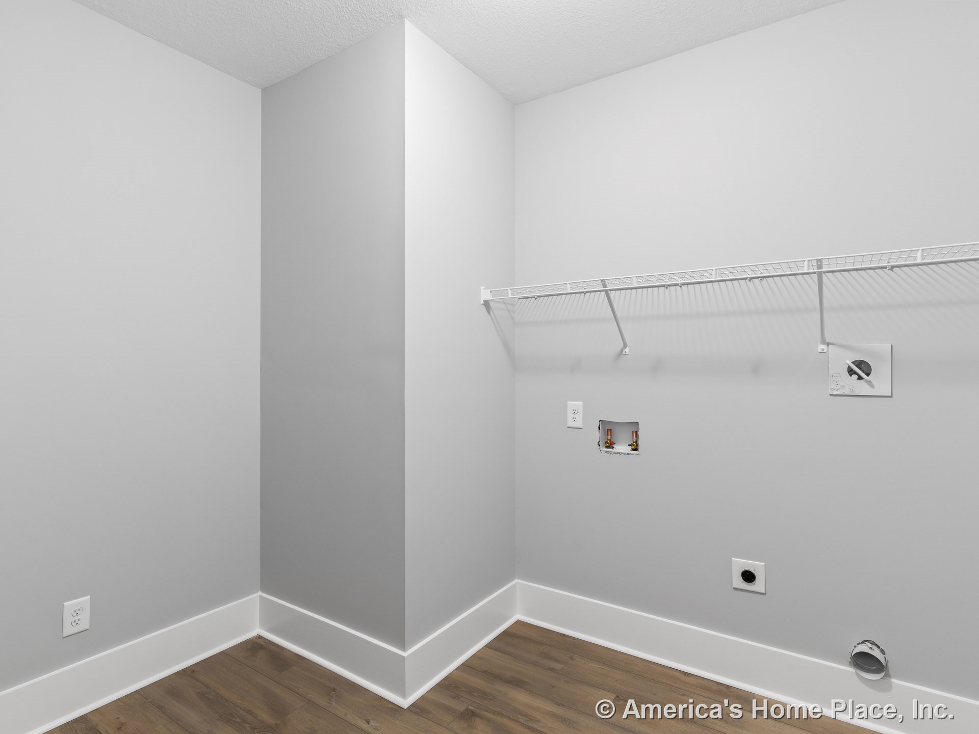 Laundry room with washer and dryer hookups, white wire shelving mounted above, light gray painted walls, wood-look plank flooring, white baseboard trim, and utility wall outlets.
