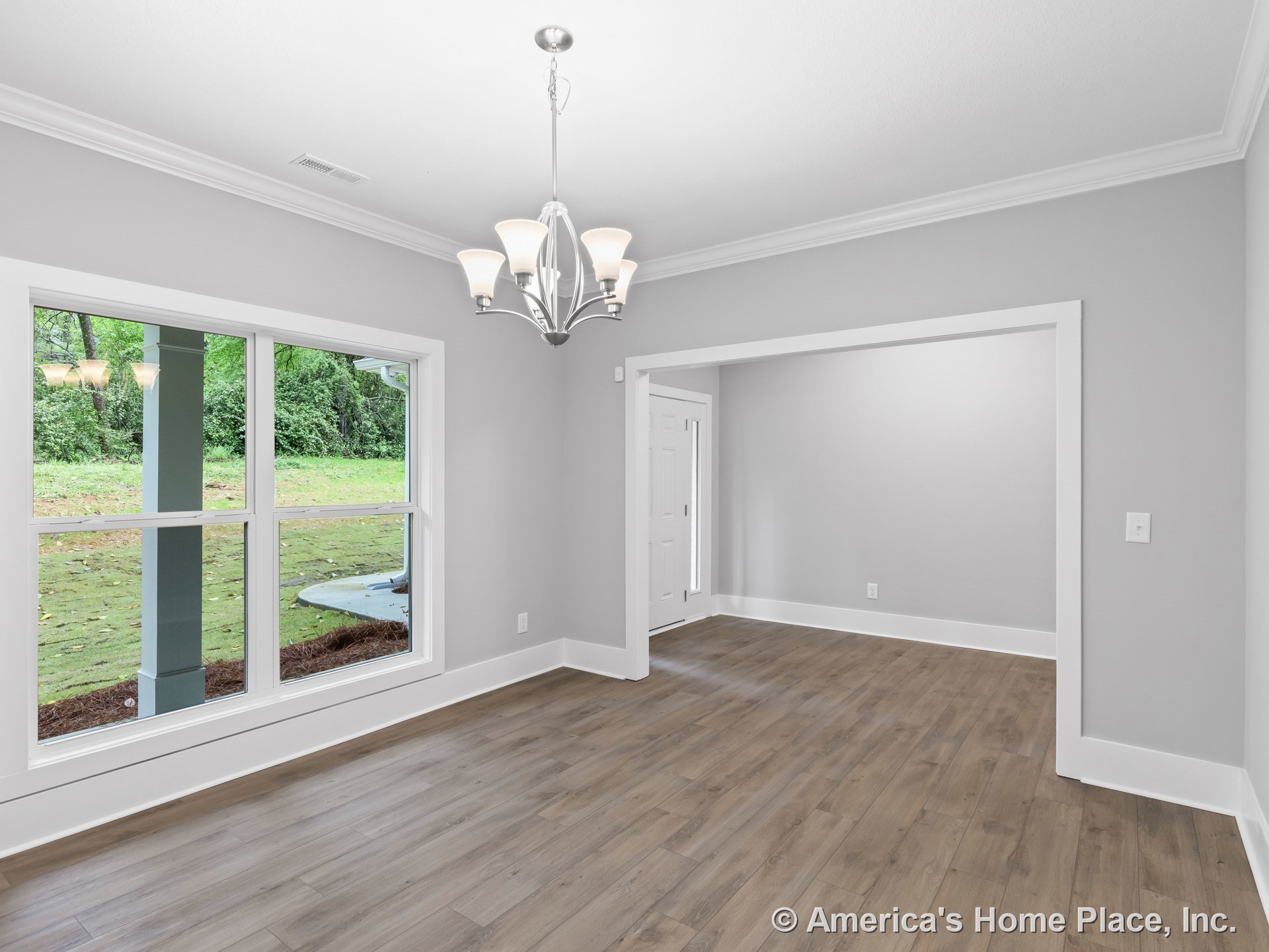 Dining area with wide double windows, gray painted walls, wood-look flooring, white trim and baseboards, crown molding, modern chandelier, and open entryway to foyer.
